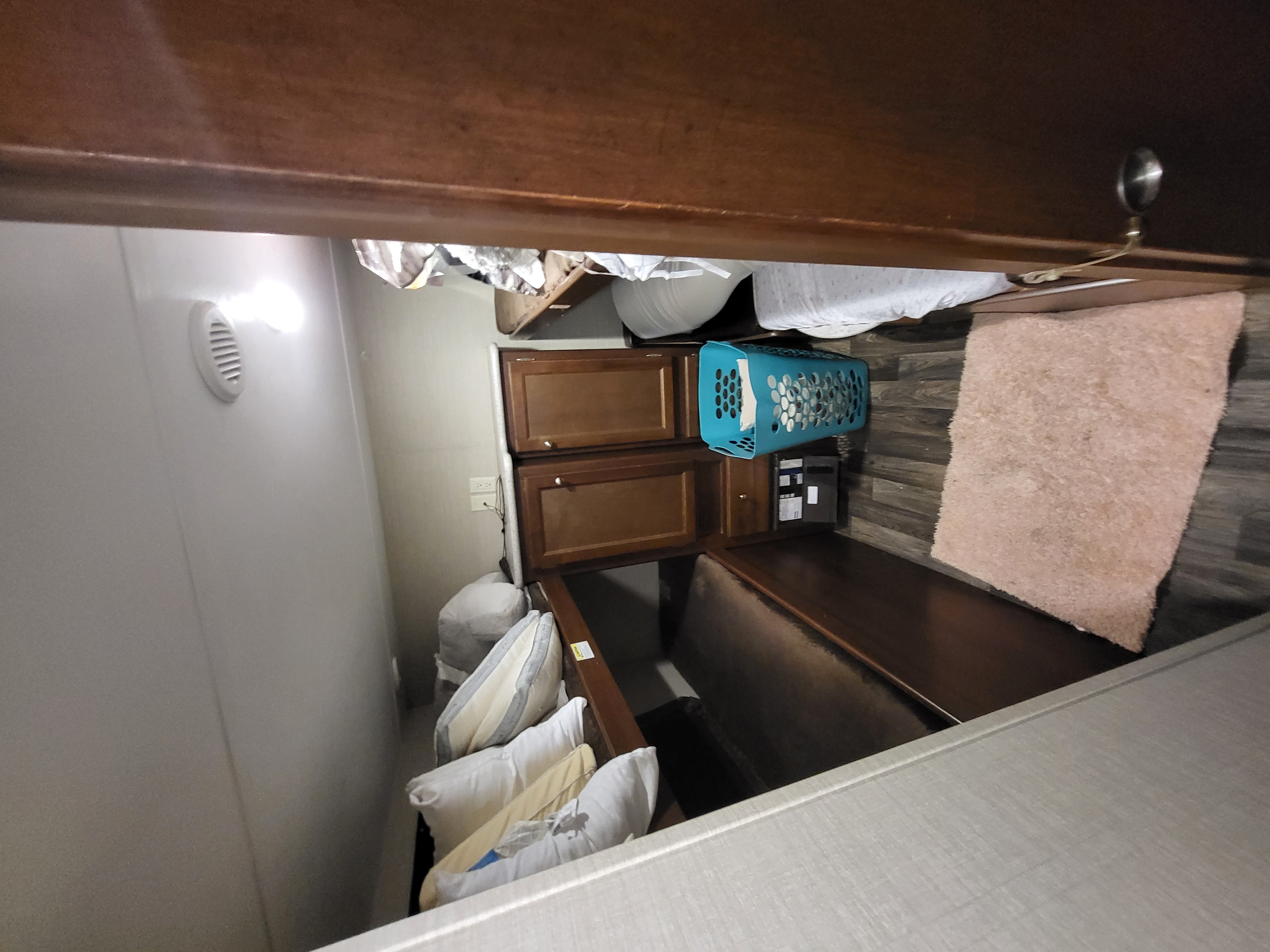 An RV rental interior showing wood cabinets, a bunk area with stored pillows, and a blue laundry basket on wood-look flooring.. Keystone RV Bullet Ultra Lite 2016