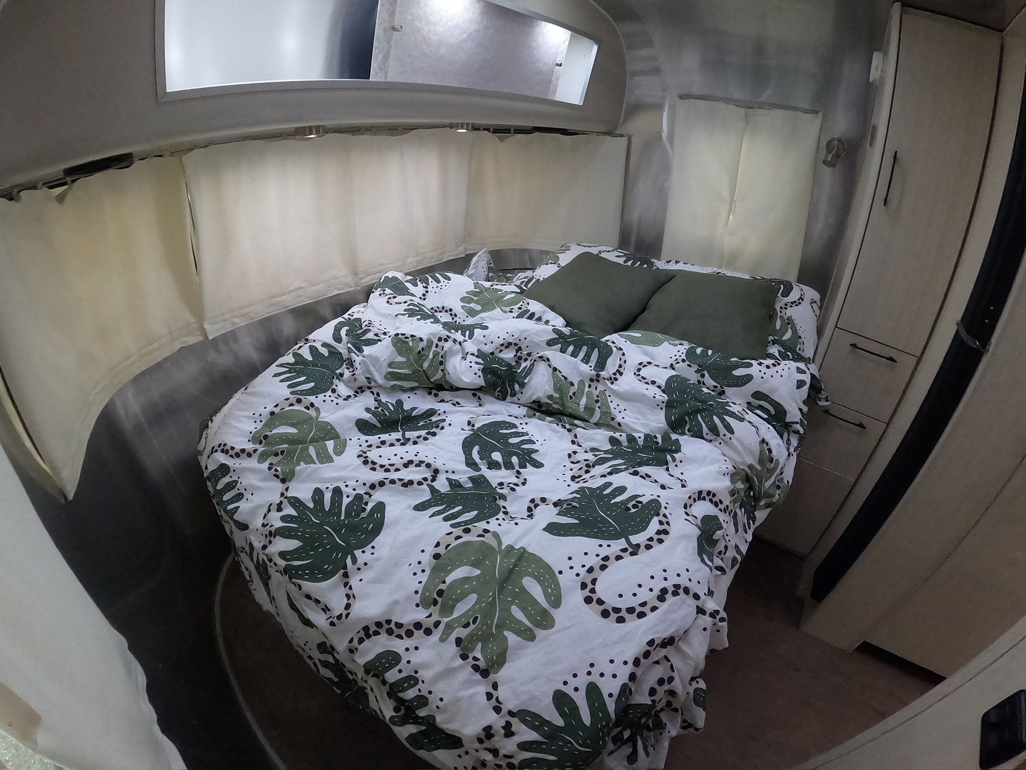 Cozy RV rental bedroom with white and green leaf-patterned bedding, green pillows, and sleek curved aluminum walls.. Airstream International 2015