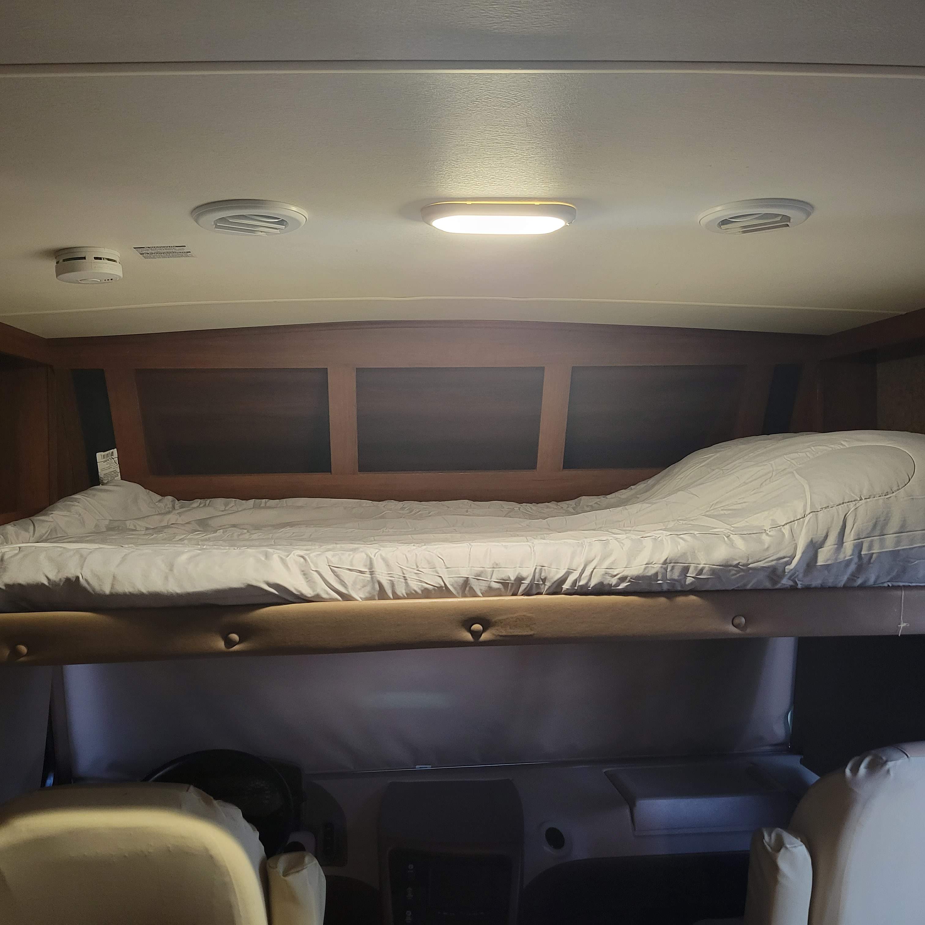 Inside an RV rental: a cozy cab-over sleeping area with white bedding above the driver's cockpit.. Forest River Fr3 2015