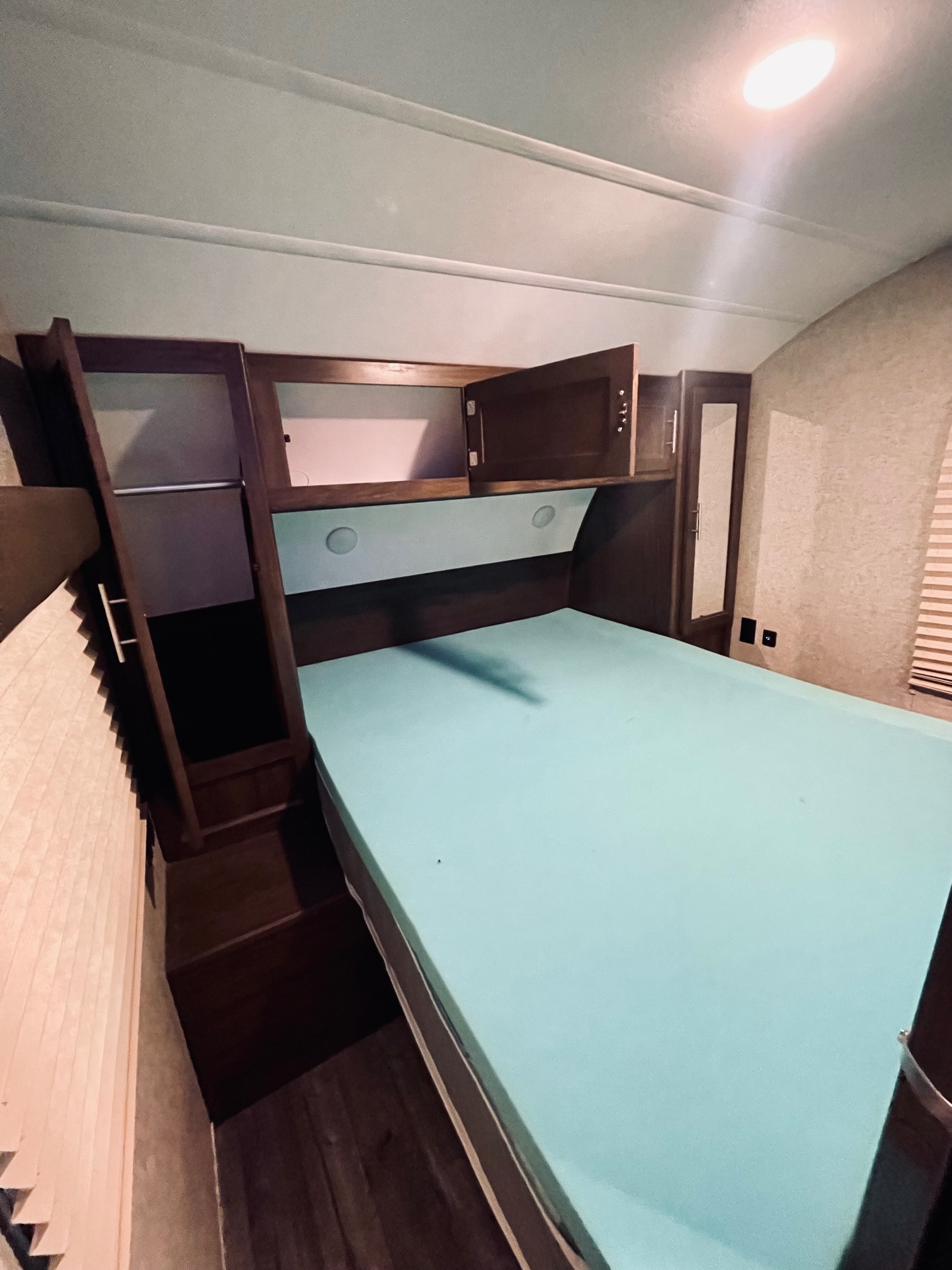 RV rental bedroom interior with light blue bed, overhead cabinets, and wardrobe. Compact sleeping area.. Forest River Cherokee Grey Wolf 2018