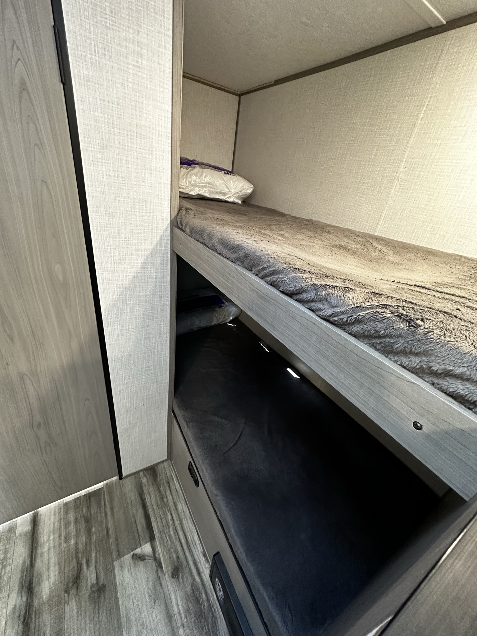 Interior view of an RV rental showing stacked bunk beds with fluffy blankets and light wood finishes.. Dutchmen Coleman Lantern LT 2023