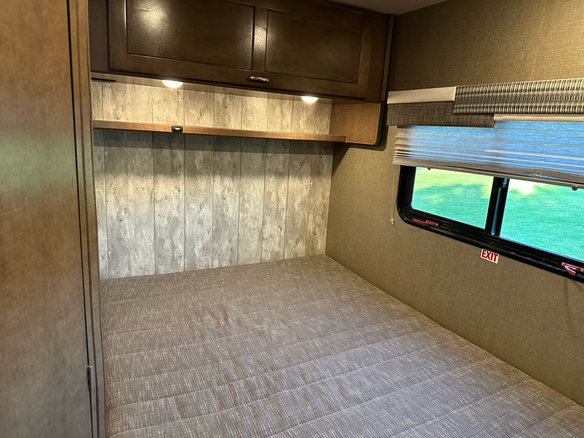 RV rental bedroom interior featuring a bed, overhead cabinets, and window with an exit sign.. Winnebago Outlook 2019