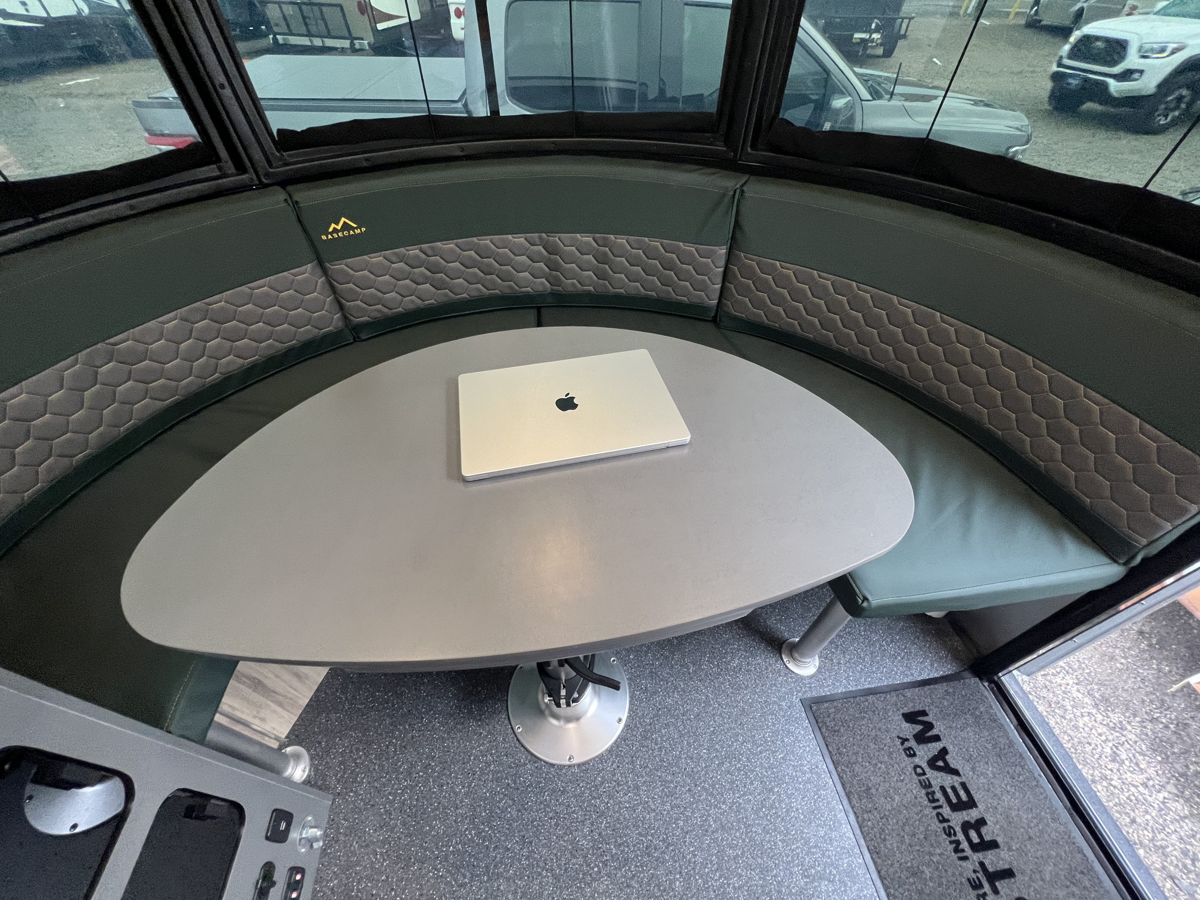 RV rental: Bright Airstream Basecamp interior featuring a curved dinette with green and gray textured seating and a MacBook.. Airstream Basecamp 2023