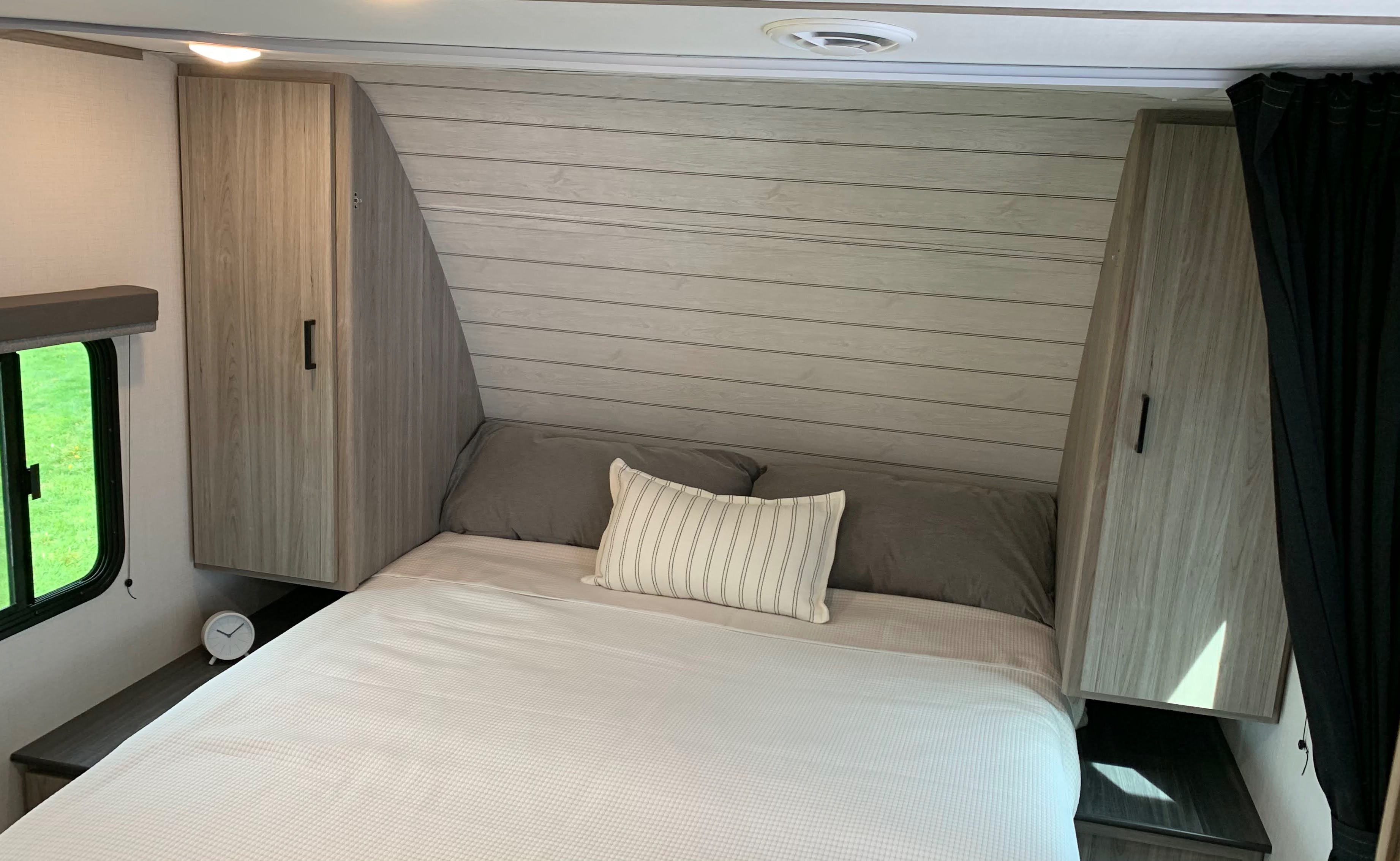 RV rental bedroom showcasing a neat bed, light wood-grain storage cabinets, and a shiplap-style accent wall.. Keystone RV Passport SL 2022