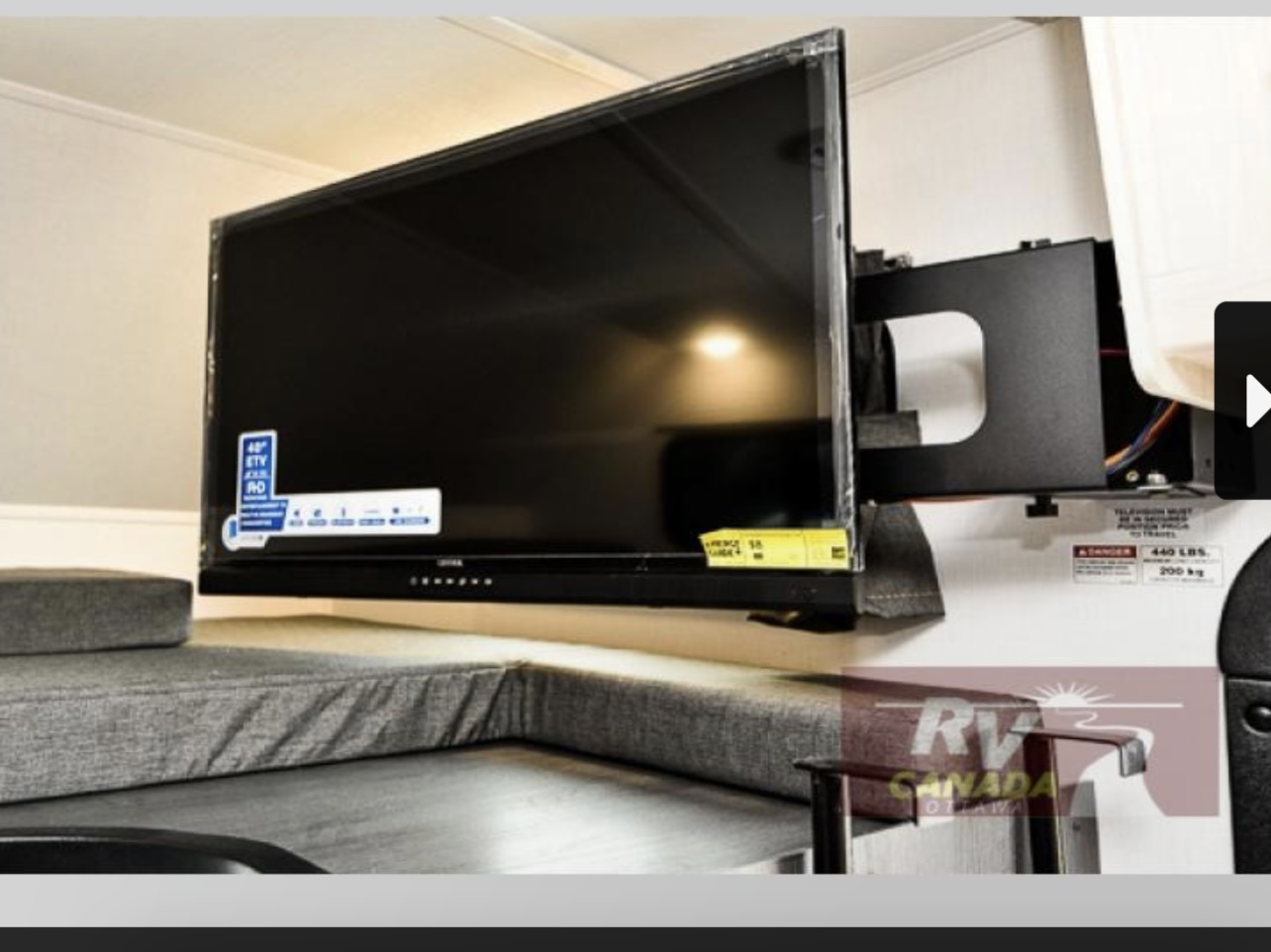 Flat-screen TV on articulating mount extends over gray upholstered seating in an RV rental interior, perfect for leisure.. Forest River Sunseeker LE 2023