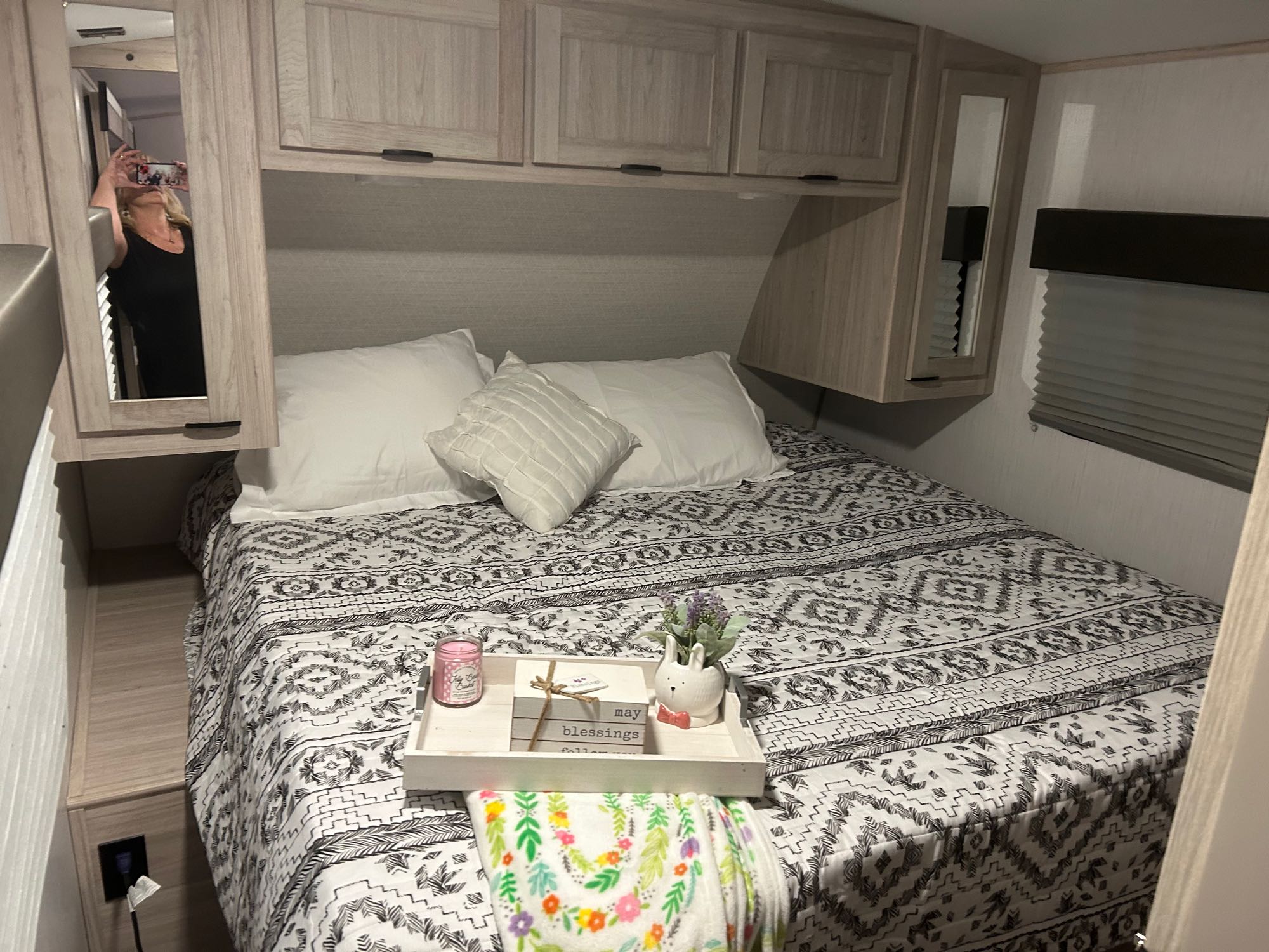 Inviting RV rental bedroom: patterned bed, white pillows, decor on tray, overhead cabinets. Photographer's reflection visible.. Thor Sun cruiser 2023