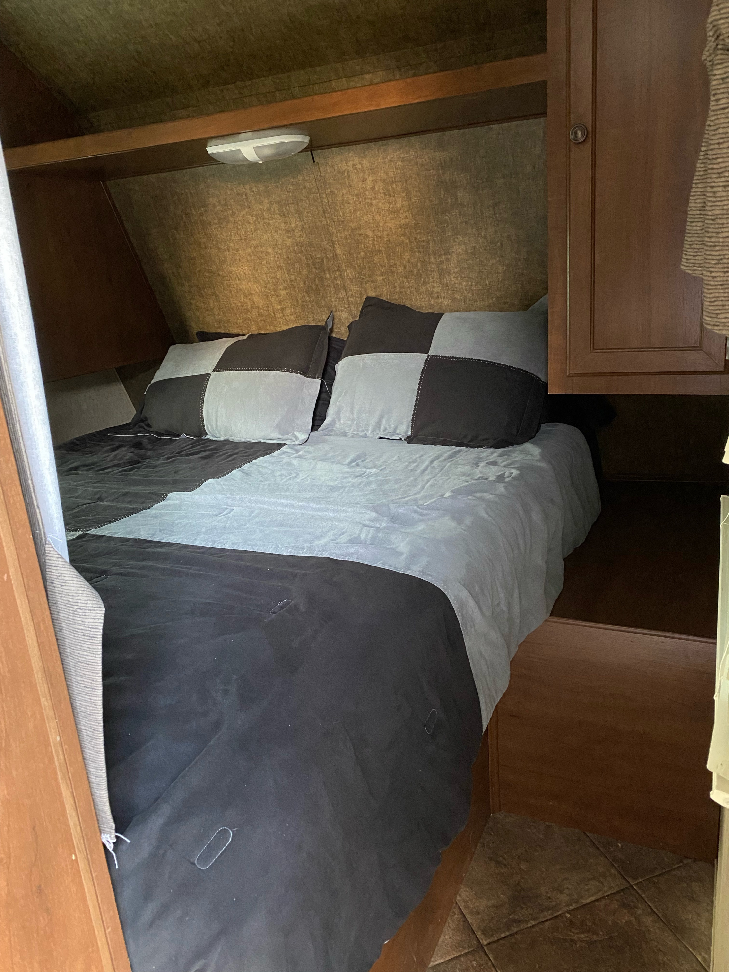 Cozy RV rental bedroom with a checkered bed, wooden cabinet, and shelf, ideal for comfortable travel.. Heartland RVs 30LX 2014