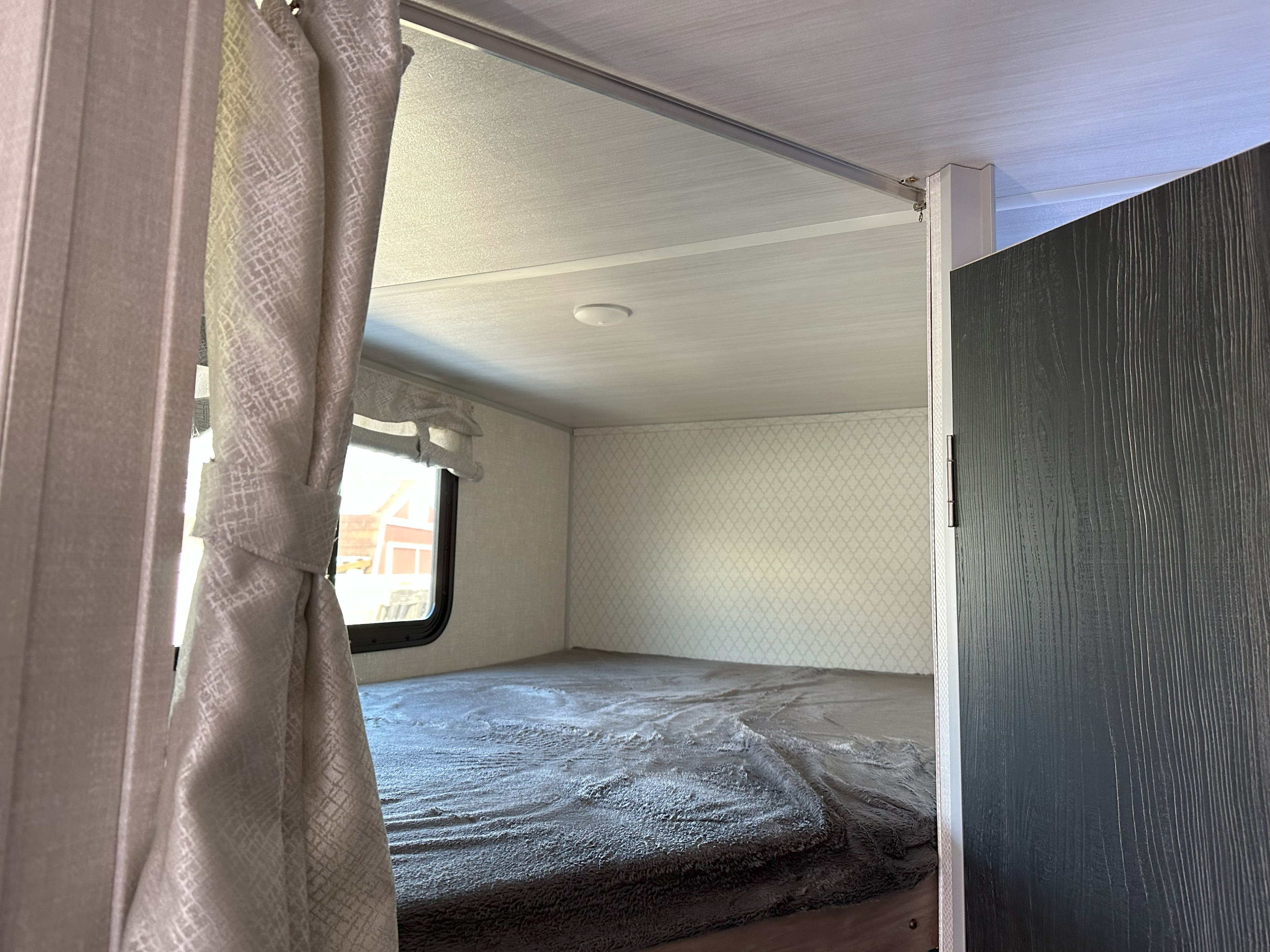 View of a comfy bunk bed in an RV rental, with a gray textured blanket, light patterned walls, and a privacy curtain.. No Boundaries 19 2022