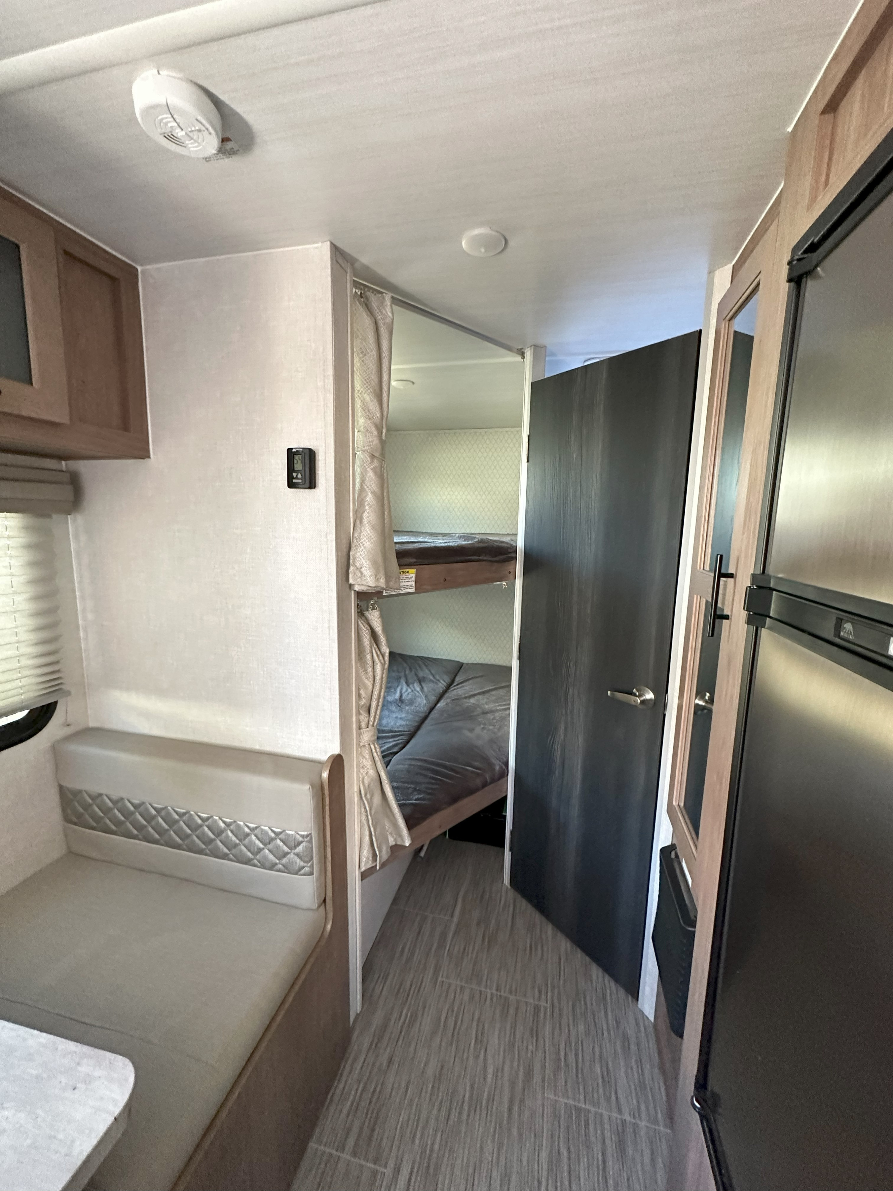 This RV rental interior features a dinette, bunk beds with privacy curtain, and a refrigerator. Ideal for adventures.. No Boundaries 19 2022
