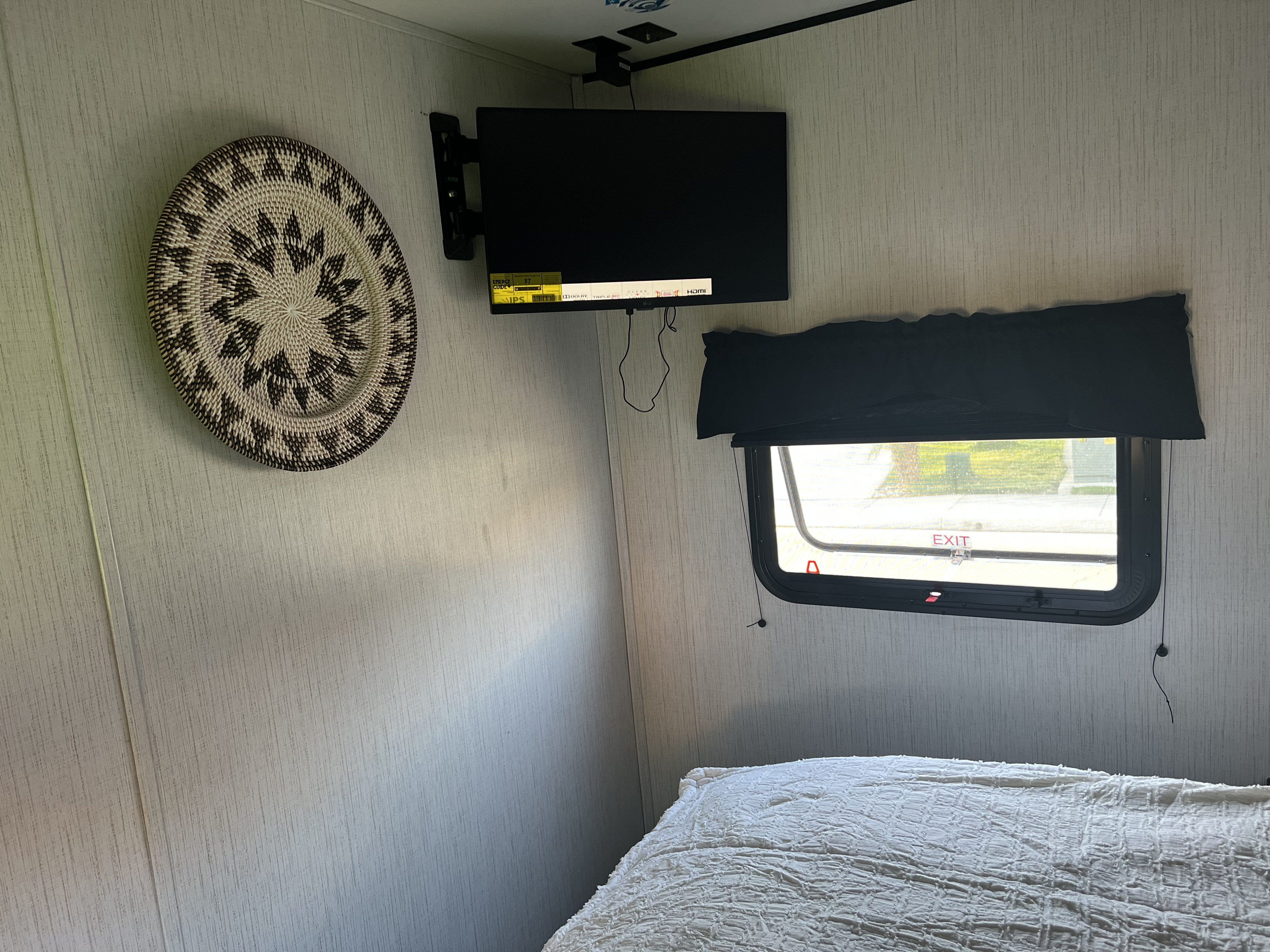 RV rental interior: A compact bedroom with a wall-mounted TV, woven basket decor, and window by the bed.. Heartland RVs Prowler 2022