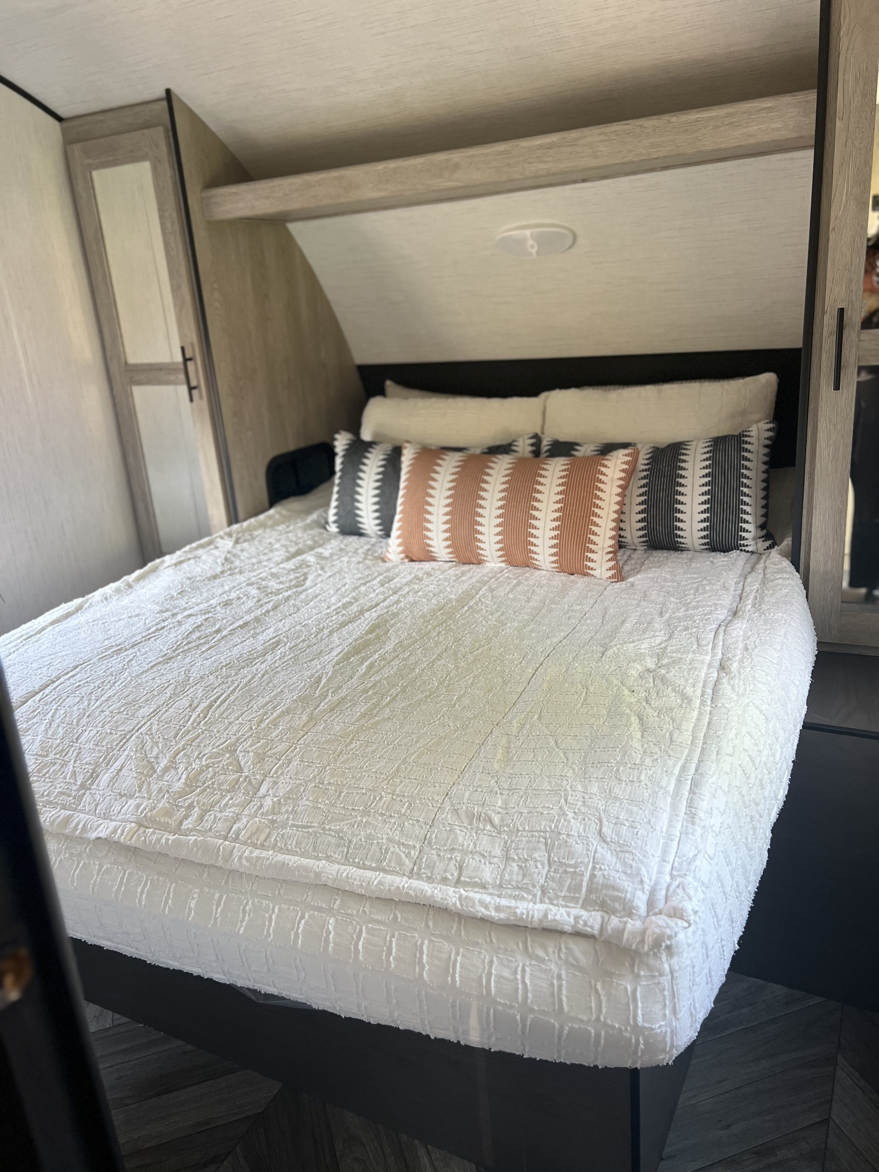 Inside a modern RV rental: a comfortable bedroom with light wood walls, a large bed, and patterned accent pillows.. Heartland RVs Prowler 2022