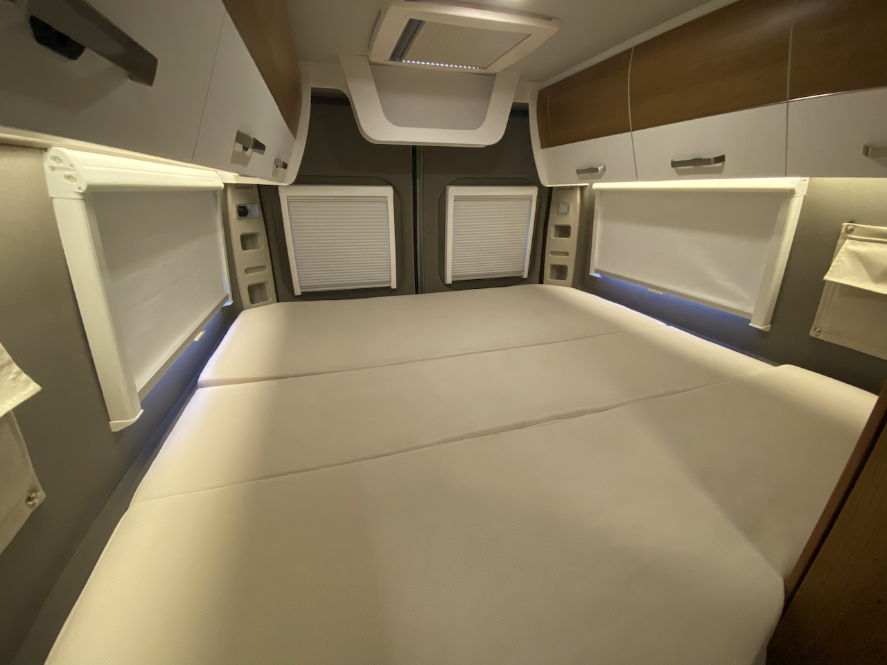 RV rental's clean, modern bedroom: A segmented mattress, pull-down window shades, and overhead storage provide comfort.. VANTourer 600L 2022