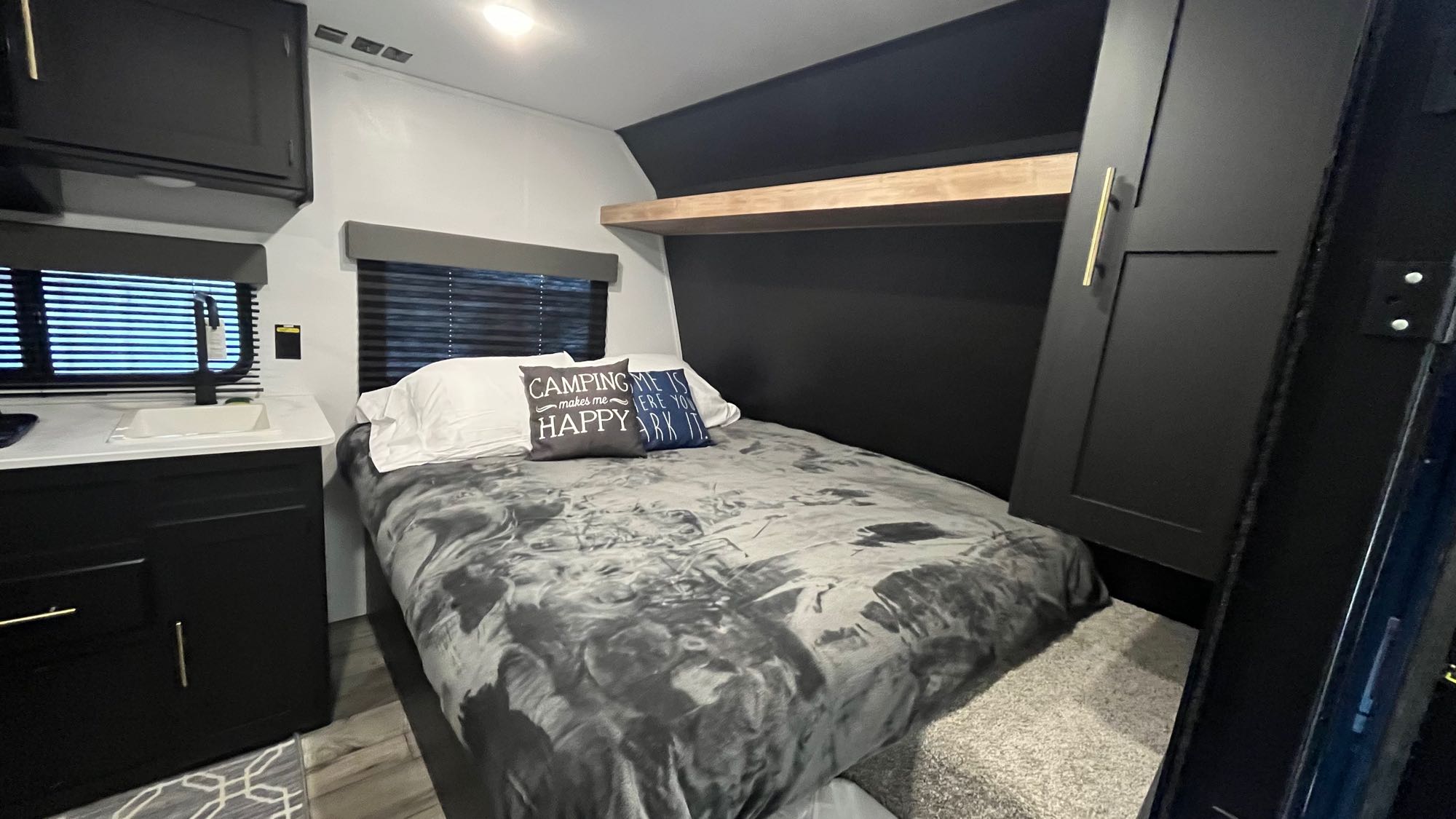 Cozy RV rental bedroom with modern black cabinetry, a comfortable bed, and a small kitchenette. Perfect for your next adventure.. Keystone RV Springdale 2022