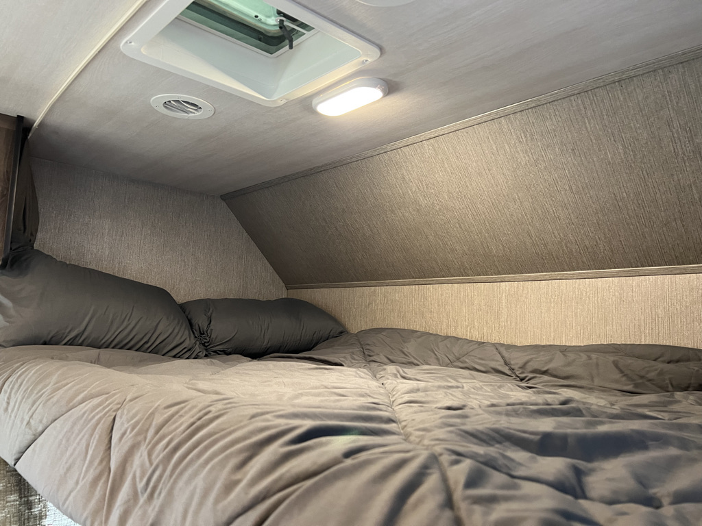 Cozy RV rental sleeping area featuring a bed with grey bedding, overhead vent, and reading light.. Nexus Triumph 23T 2020
