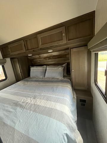 An RV rental bedroom featuring a bed with blue and grey striped bedding, wood overhead cabinets, and side windows.. Gulf Stream Kingsport 2021