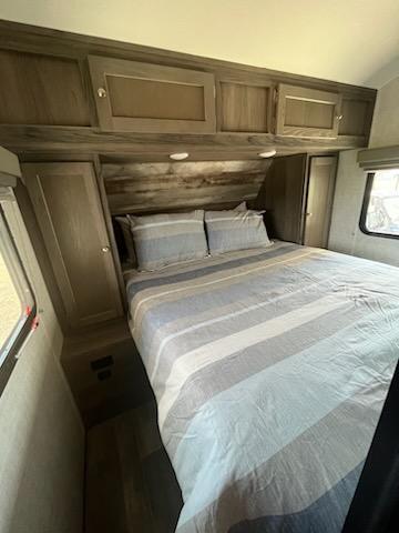 RV rental bedroom: a queen bed with striped bedding, overhead cabinets, side storage, dark wood floor, and window.. Gulf Stream Kingsport 2021