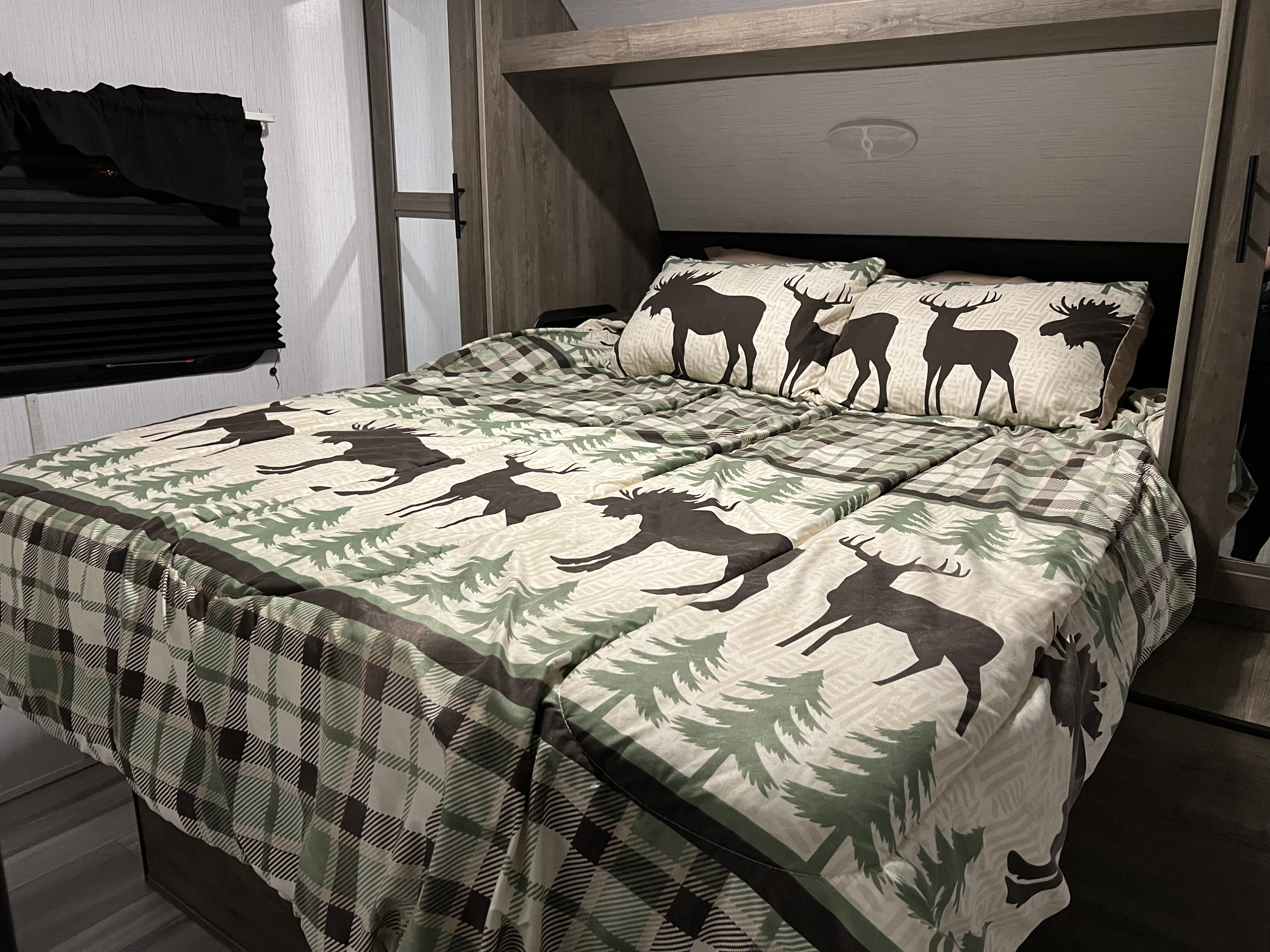 Cozy RV rental bedroom with a comfy bed, nature-themed comforter featuring deer, moose, and trees, and plaid accents.. Heartland RVs Pioneer 2023