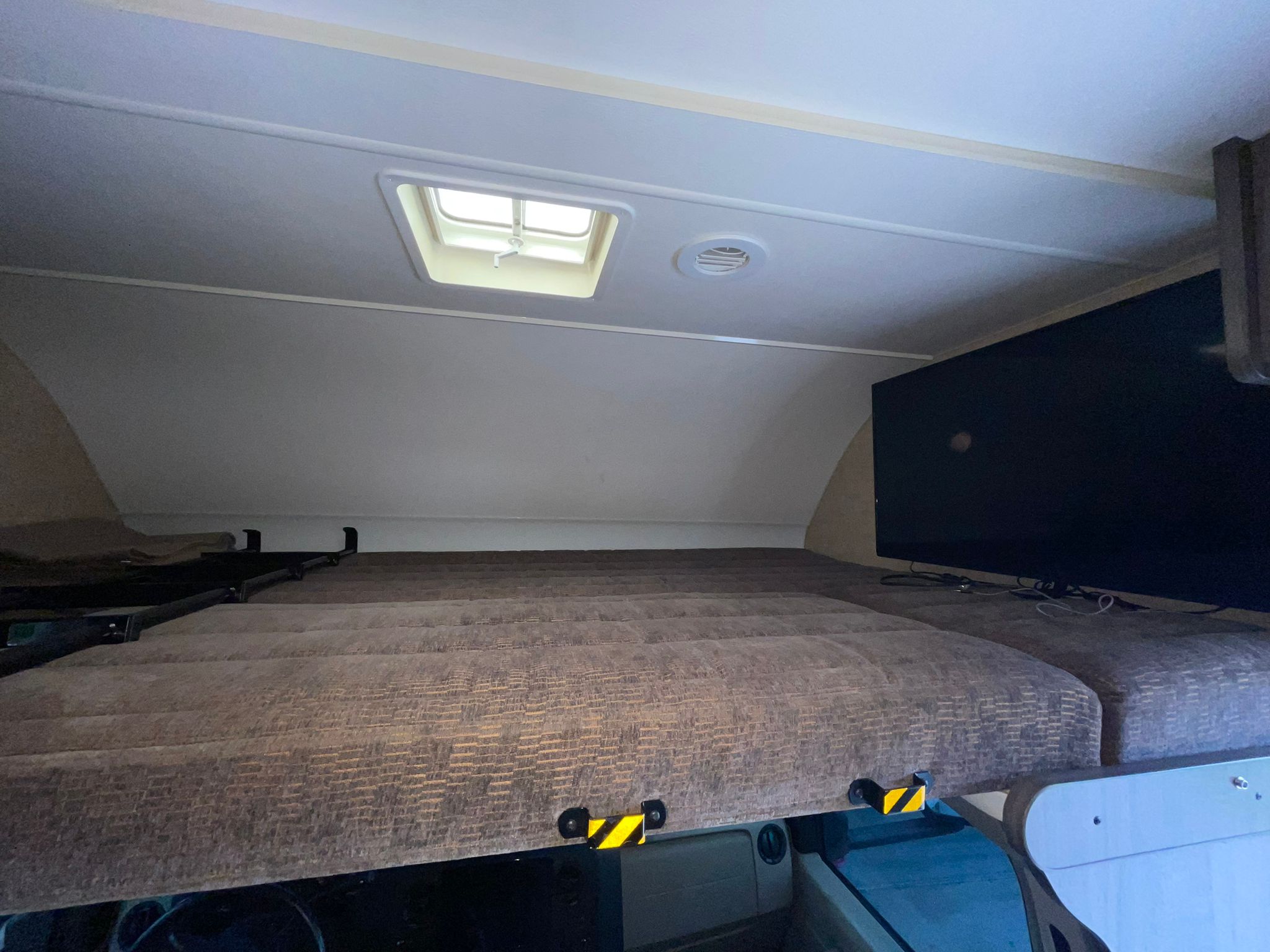RV rental's cozy cab-over sleeping bunk, featuring a mattress, skylight, vent, and TV.. Winnebago Minnie Winnie 2019