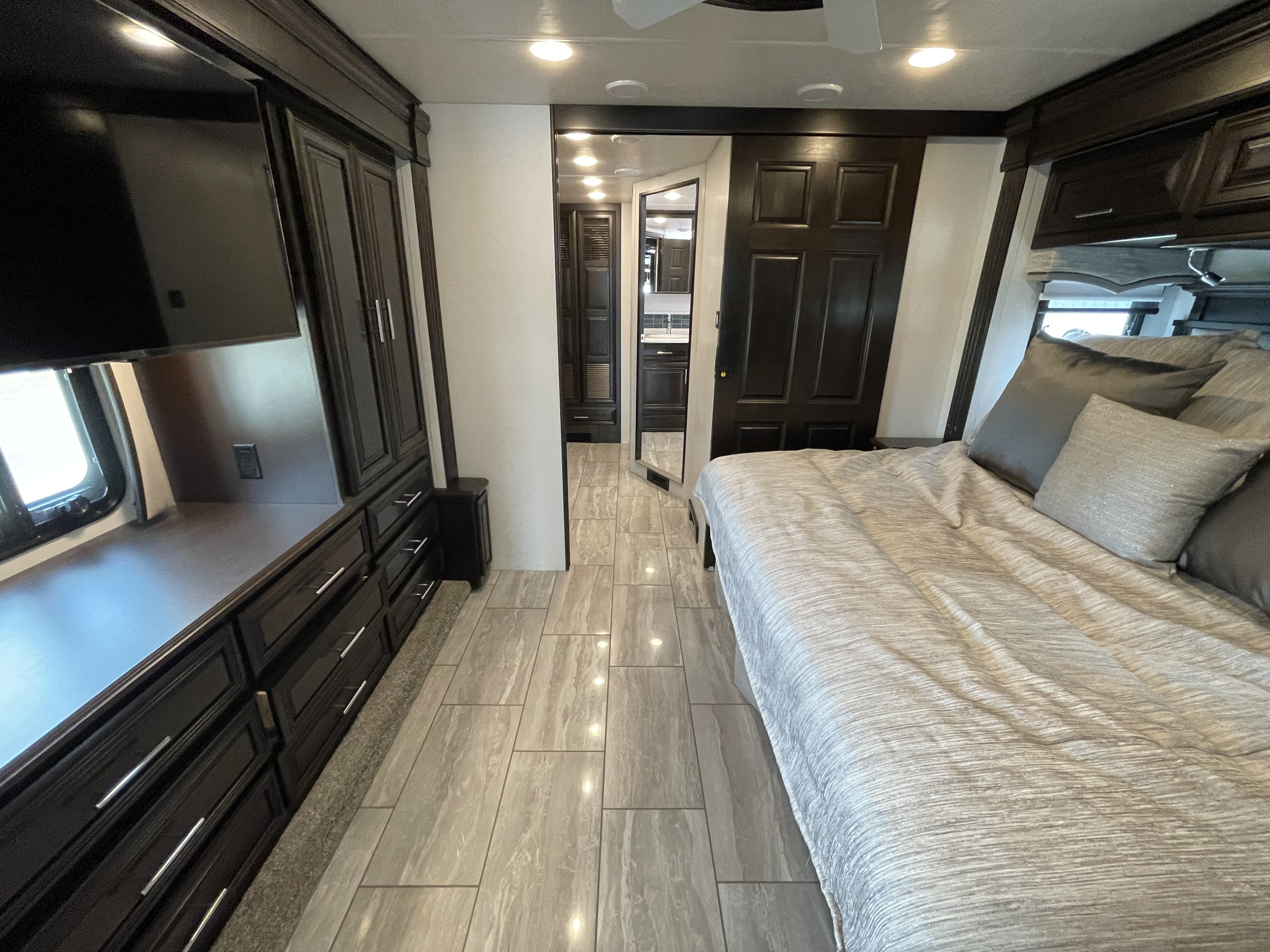 Modern RV rental bedroom with dark cabinetry, TV, comfortable bed, and stylish tile flooring. Offers ample storage.. Berkshire XLT 2023