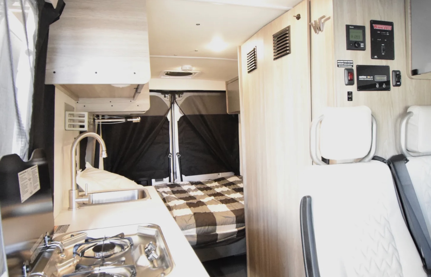 Inside this RV rental: a compact kitchenette with sink and stove, a cozy bed, and control panels for a comfortable journey.. Winnebago Solis 2022