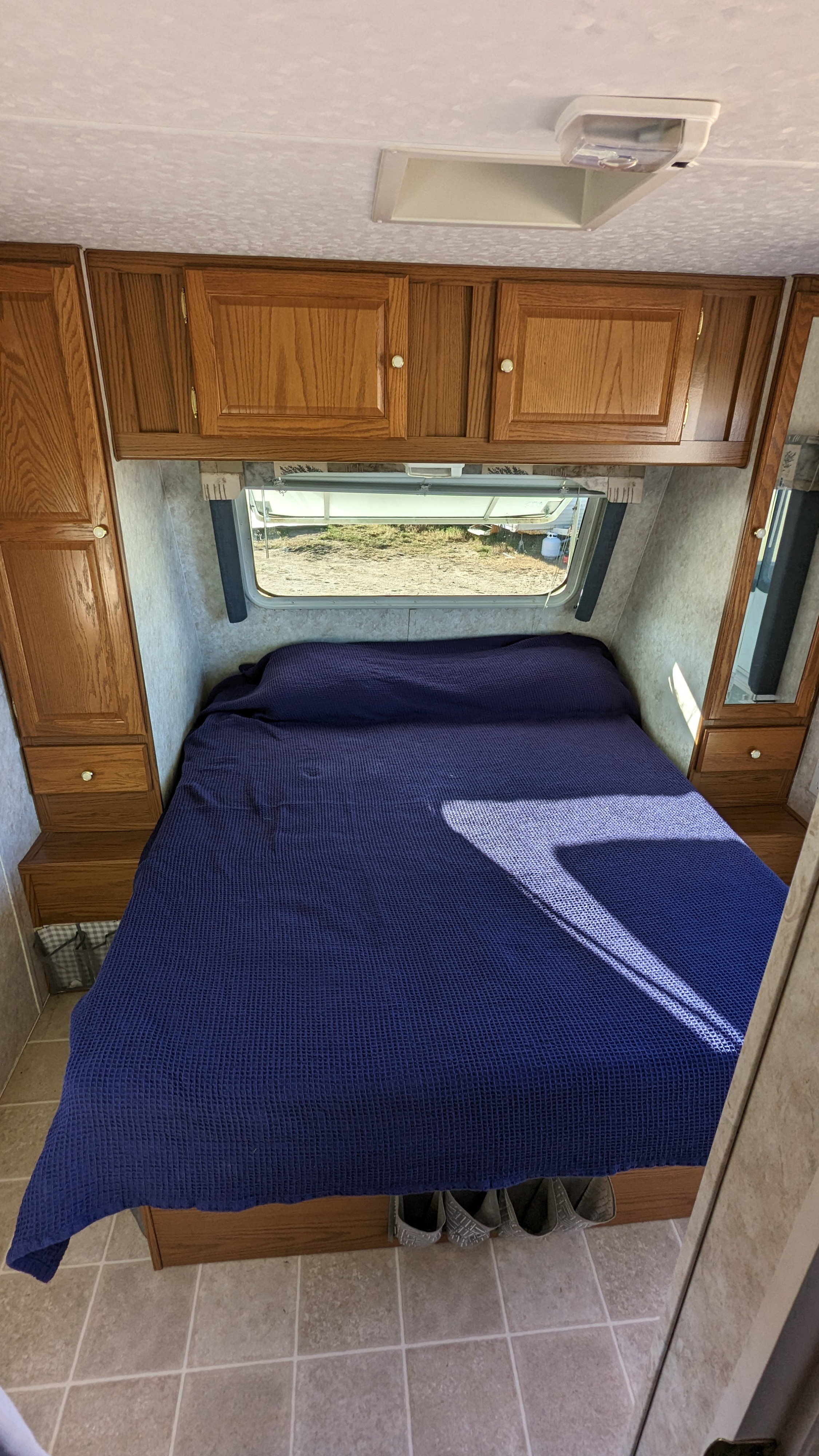 Inside an RV rental: compact bedroom with a blue bed, wood cabinets, and window view for your travel adventures.. Forest River Wildwood 2005