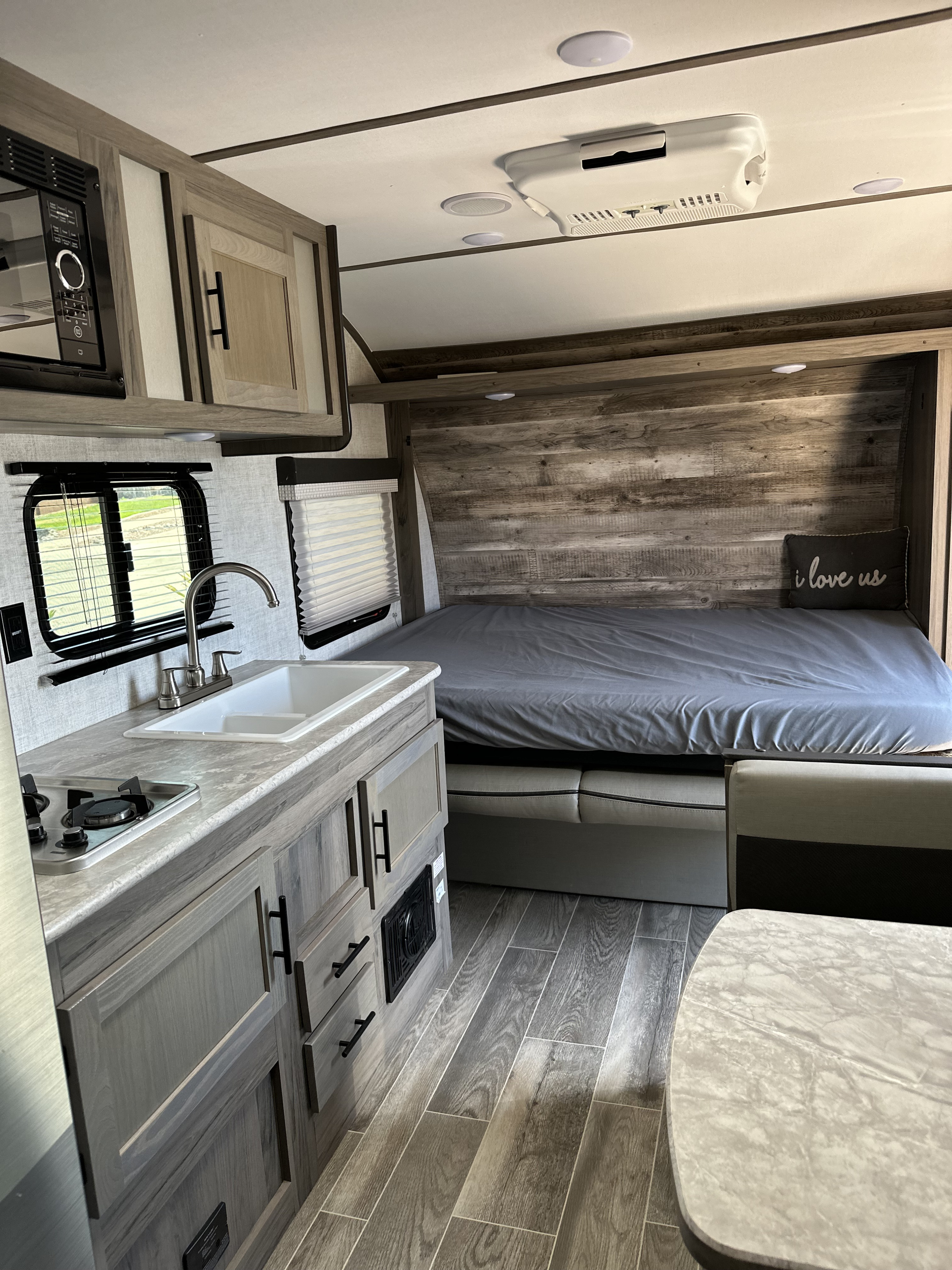 RV rental interior: A compact kitchen with microwave, sink & stove, alongside a bed & dining area in a modern travel trailer.. Gulf Stream Ameri-Lite Super Lite 2022