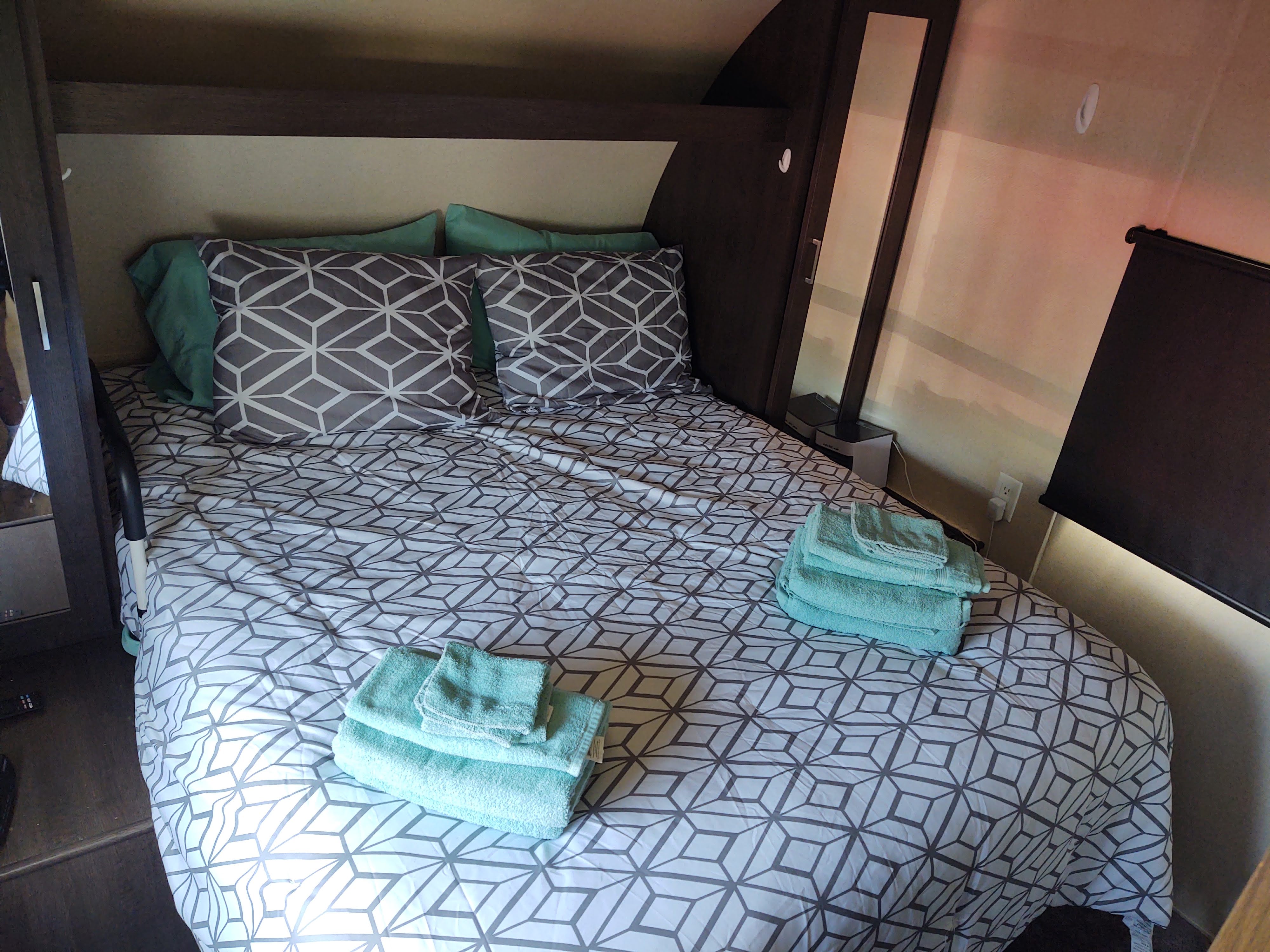 RV rental bedroom: a comfortable bed with gray geometric bedding, green pillows, and stacked aqua towels.. Forest River Salem 2019