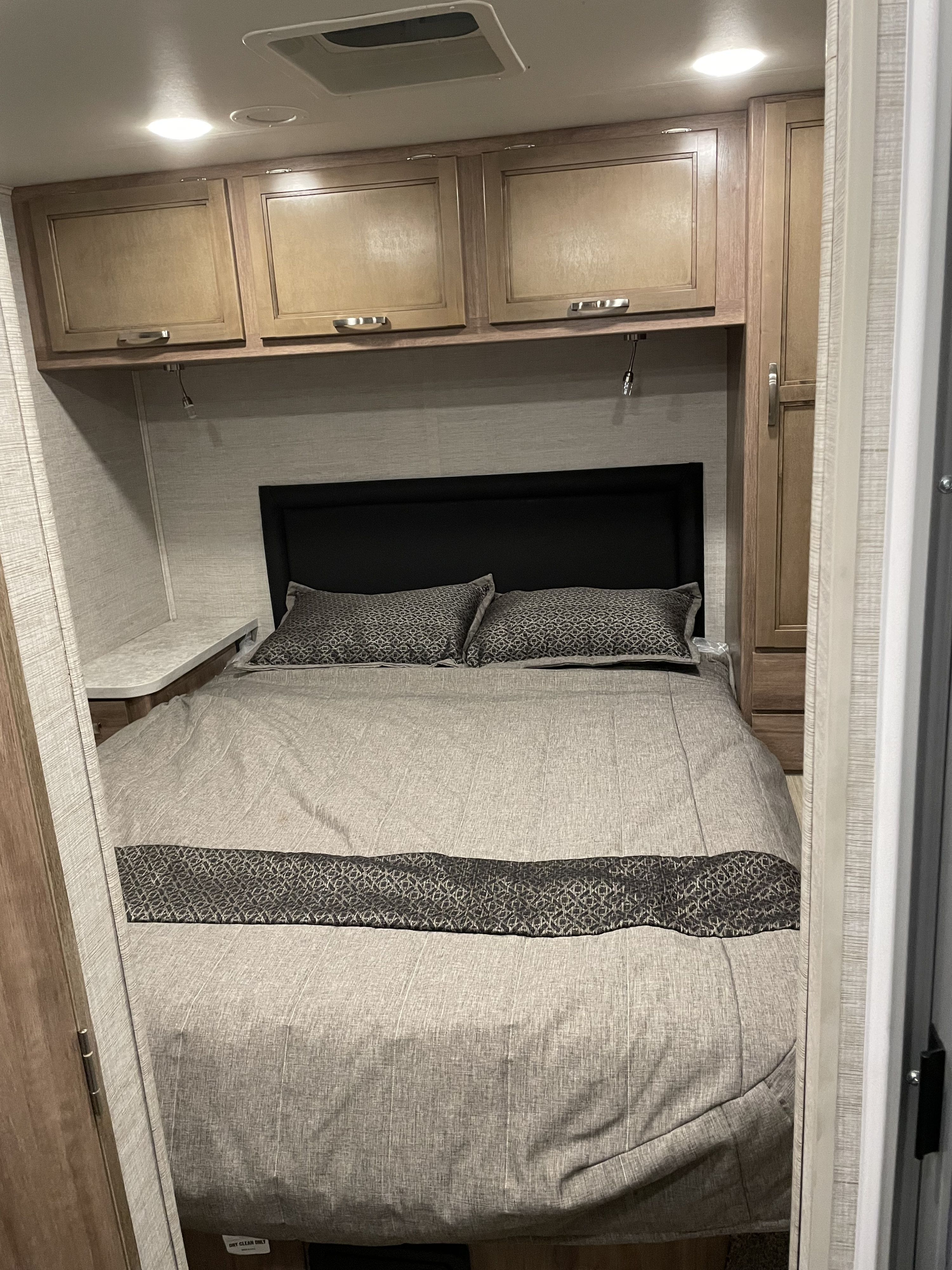 Cozy RV rental bedroom featuring a comfortable bed with gray linens, overhead cabinets, and task lighting for travel.. Jayco Redhawk SE 2021