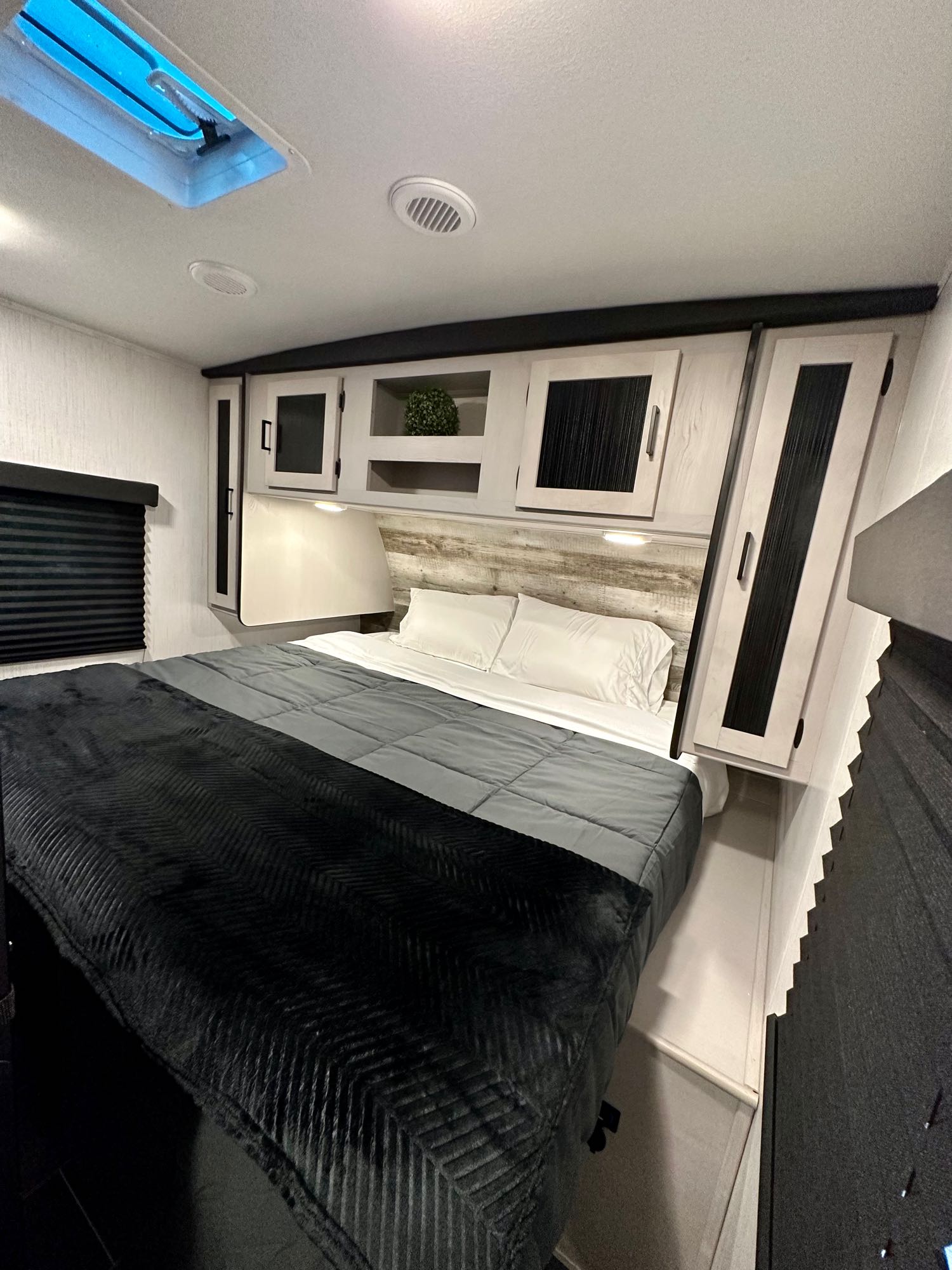 Cozy RV rental bedroom features a comfy bed with grey and black bedding, overhead storage, and a skylight. Ideal for travel.. Heartland RVs Mallard 2023