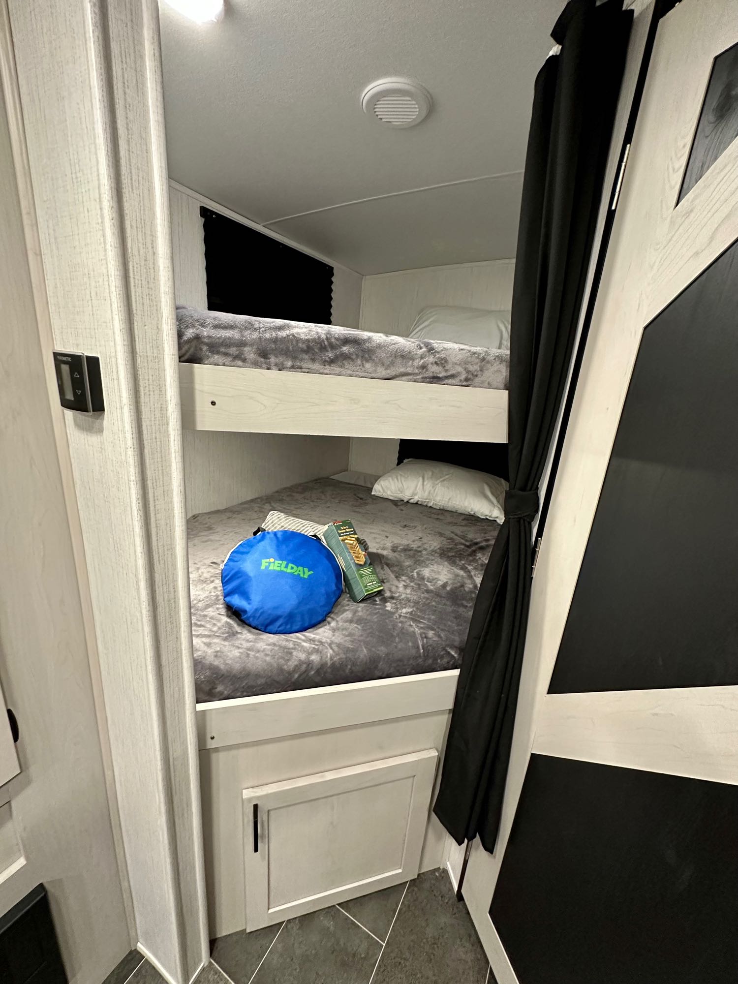 RV rental interior features clean, compact bunk beds with grey bedding, black accents, & a side control panel.. Heartland RVs Mallard 2023