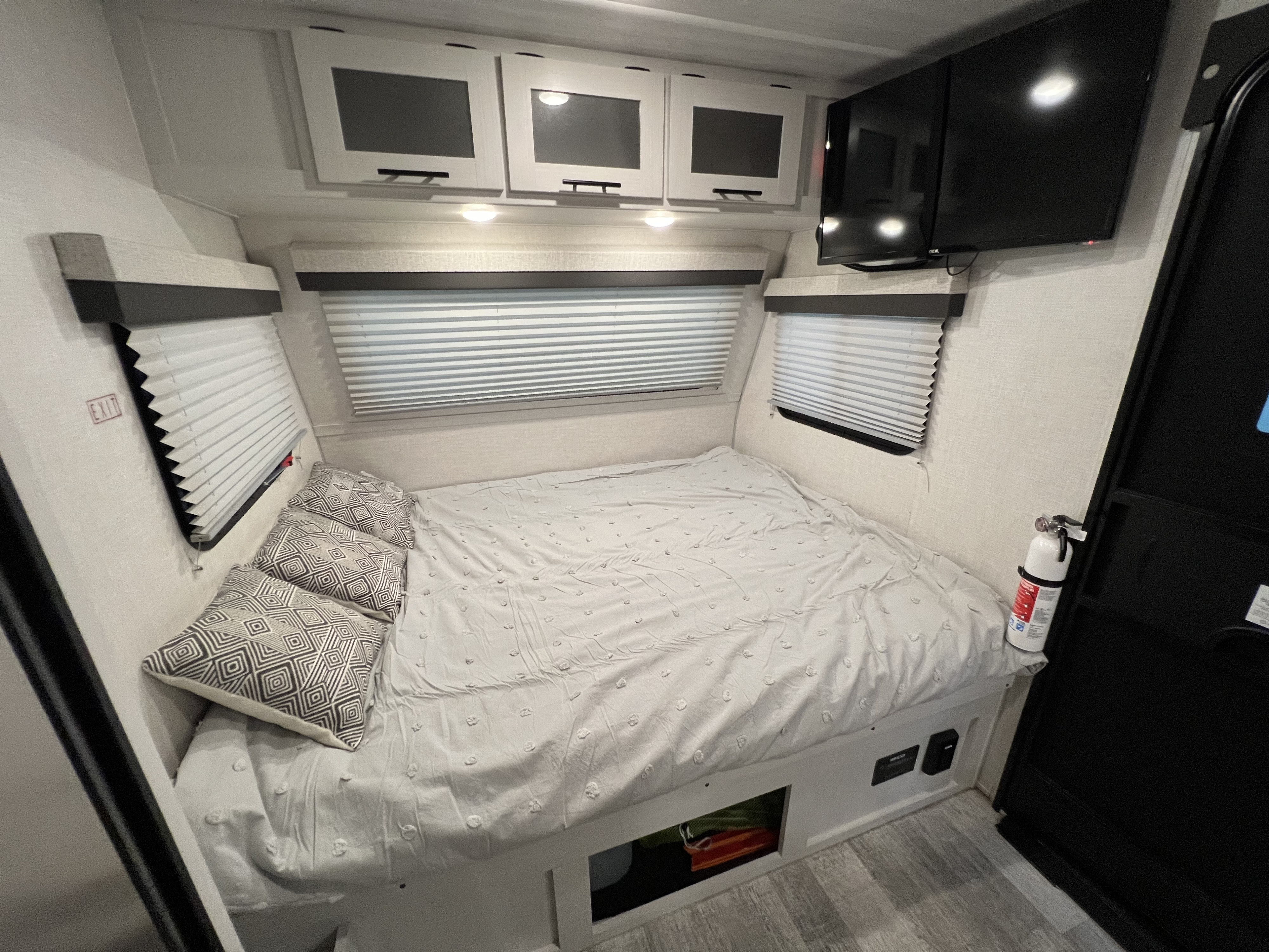 Cozy RV rental bedroom: a bed with storage, overhead cabinets, mounted TV, and fire extinguisher, ready for your travels.. No Boundaries 16 2023