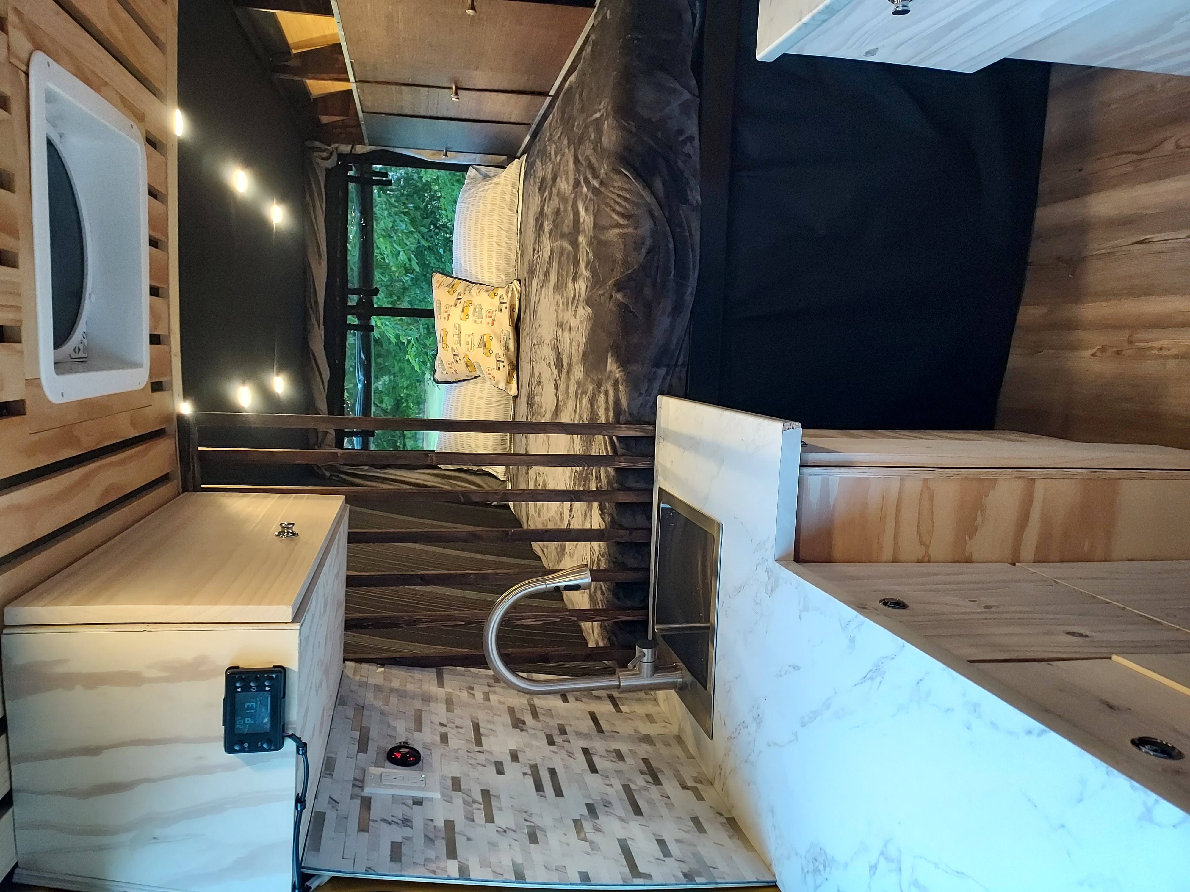 Cozy RV rental interior with a bed, compact kitchen with sink, wood paneling, string lights, and a window view.. Freightliner Sprinter 2013