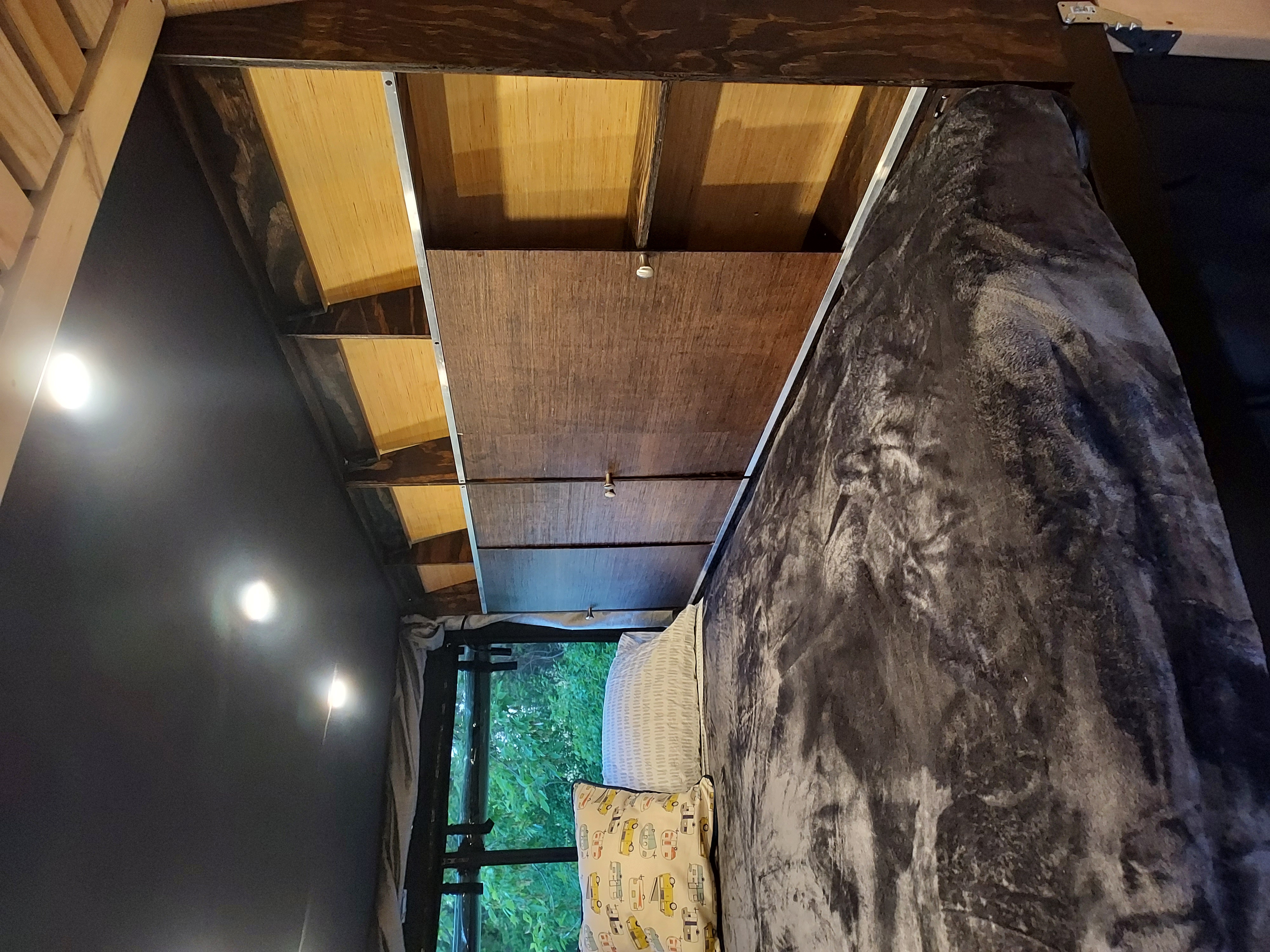 Cozy RV rental bedroom featuring a comfy bed with a plush blanket, bright lights, and overhead paneling with a window view.. Freightliner Sprinter 2013