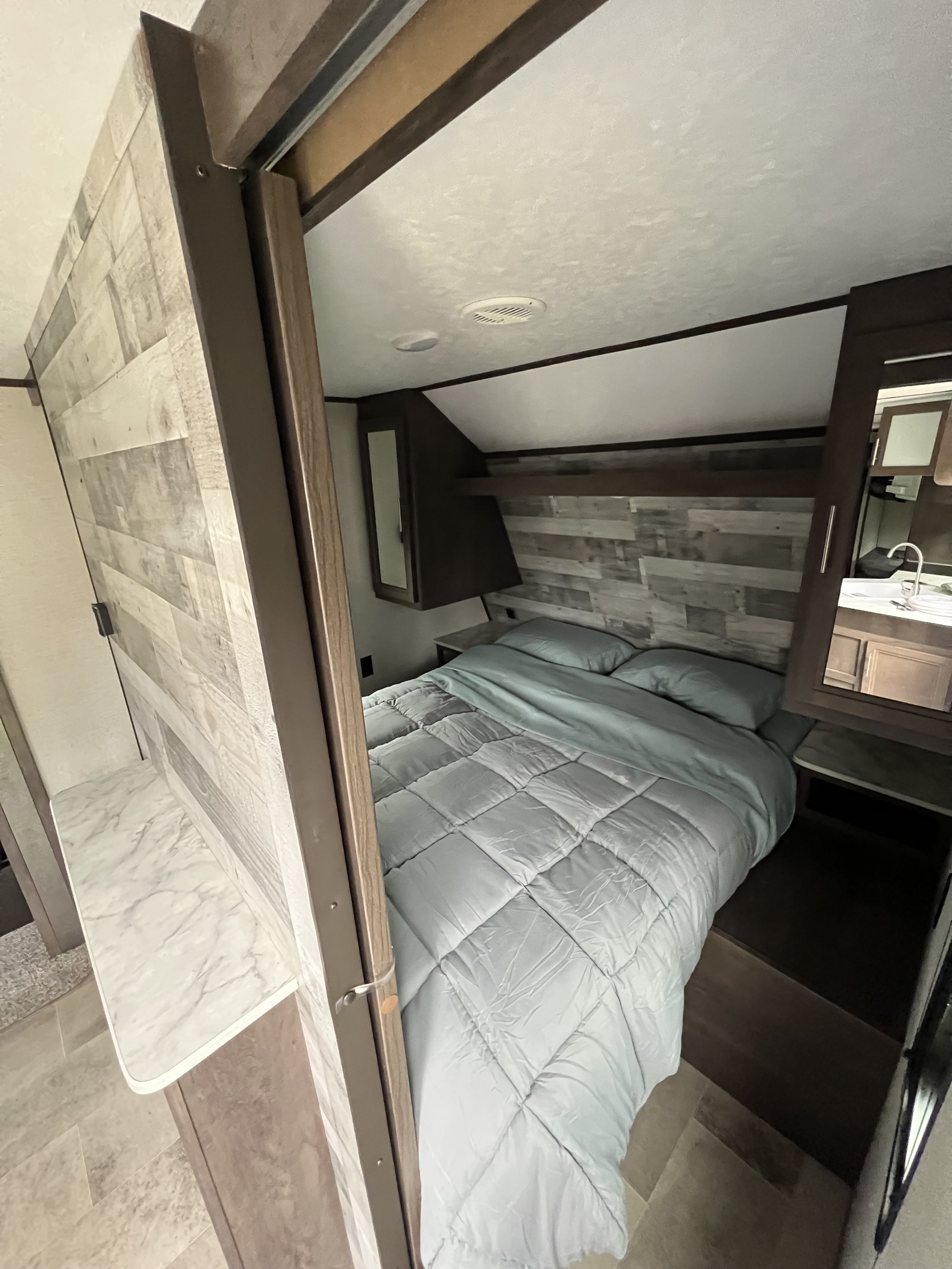 RV rental bedroom interior featuring a comfortable bed, wood-plank headboard, and compact vanity with sink.. Coleman dutchmen 2021