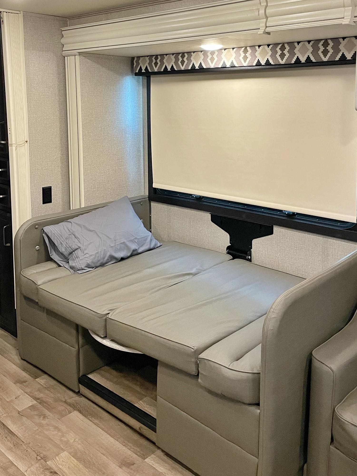 An RV rental's interior featuring a comfortable gray convertible sofa bed with pillow, window shade, and decorative valance.. Jayco Alante 2020