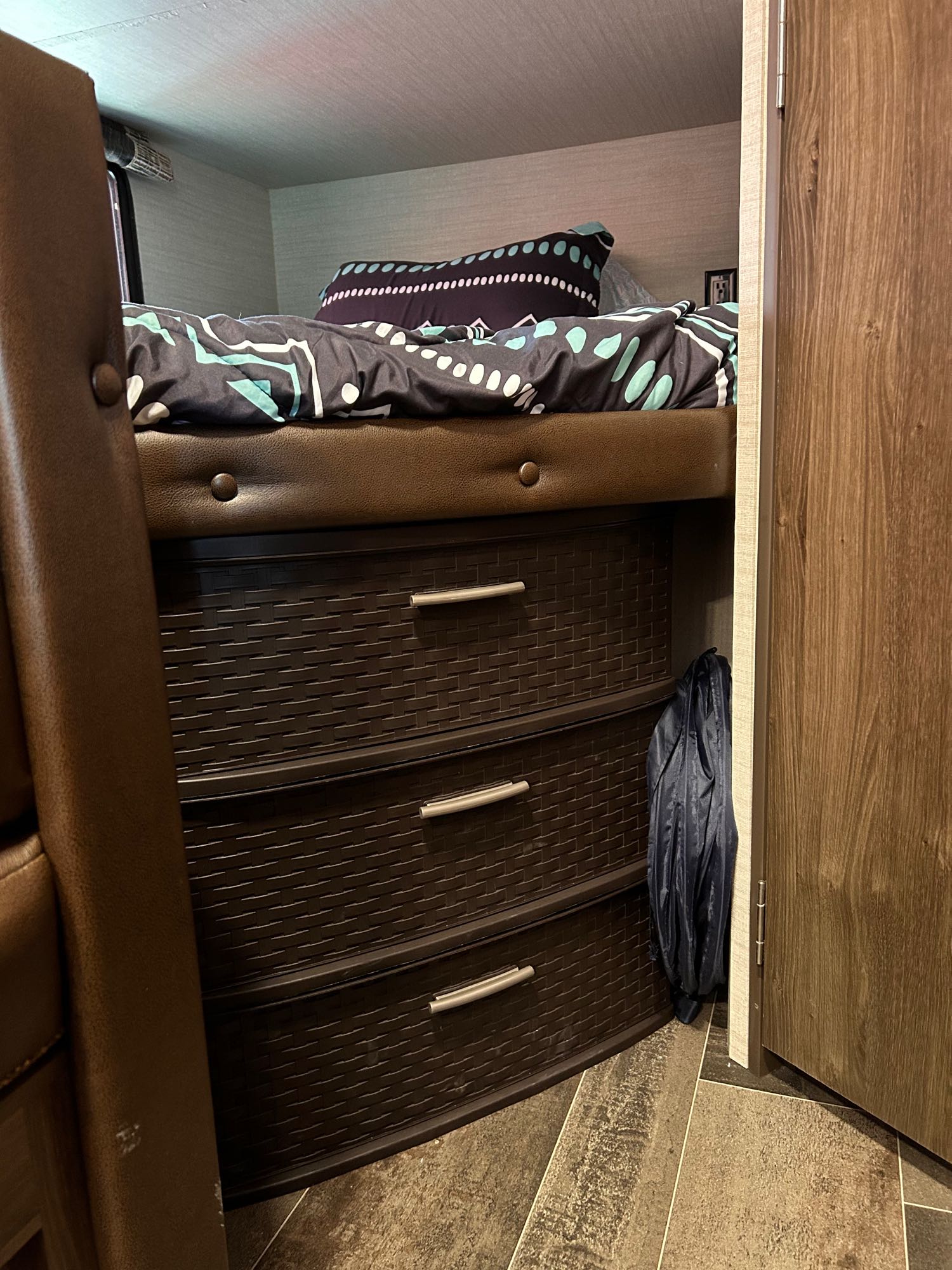 RV rental bunk/bed with patterned bedding, 3 brown wicker-style drawers, and a wooden door. A compact, organized space.. Keystone RV Bullet Crossfire 2017