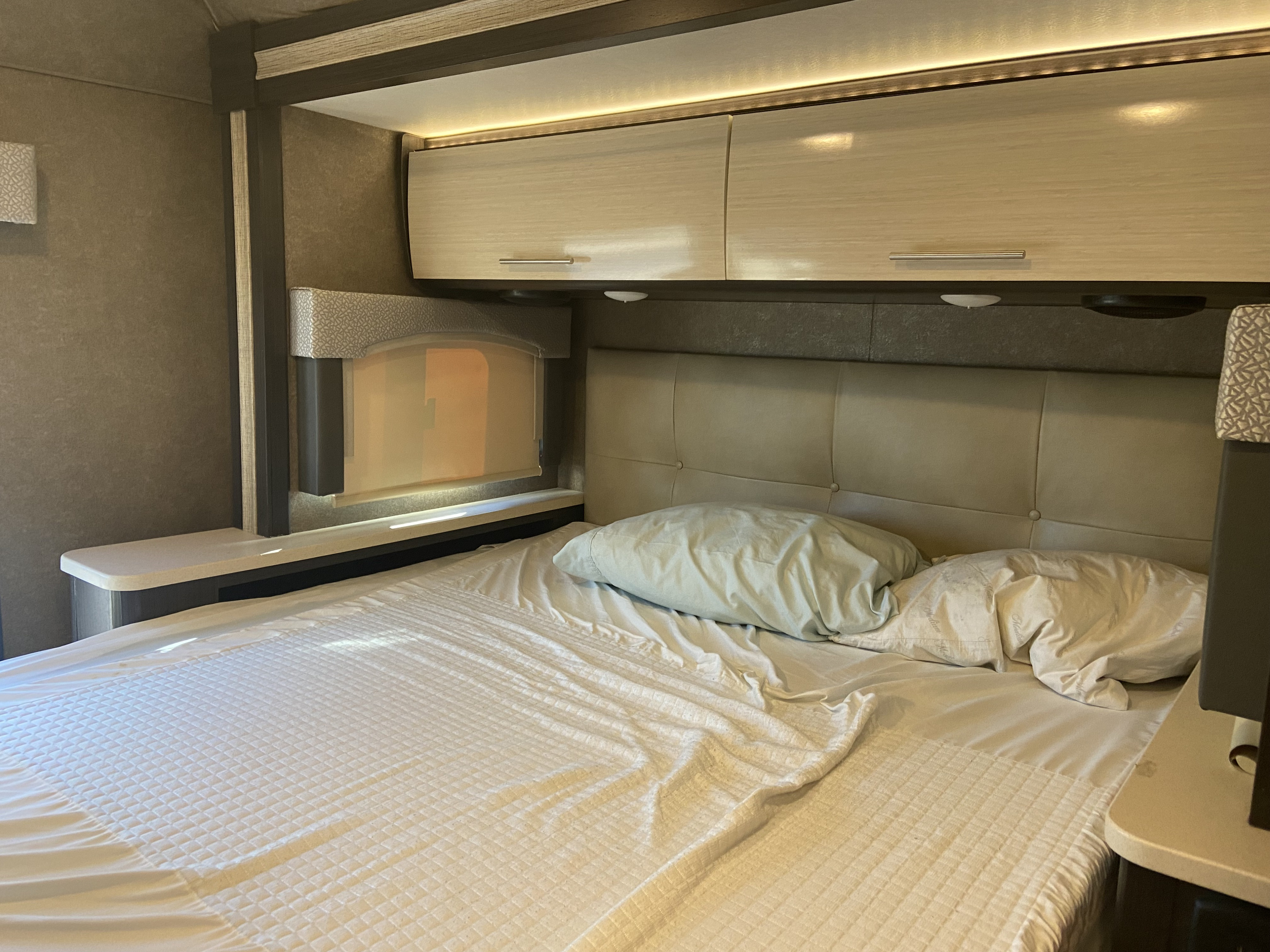 Compact RV rental bedroom: large bed, padded headboard, overhead storage with integrated lighting.. Thor Vegas 2018