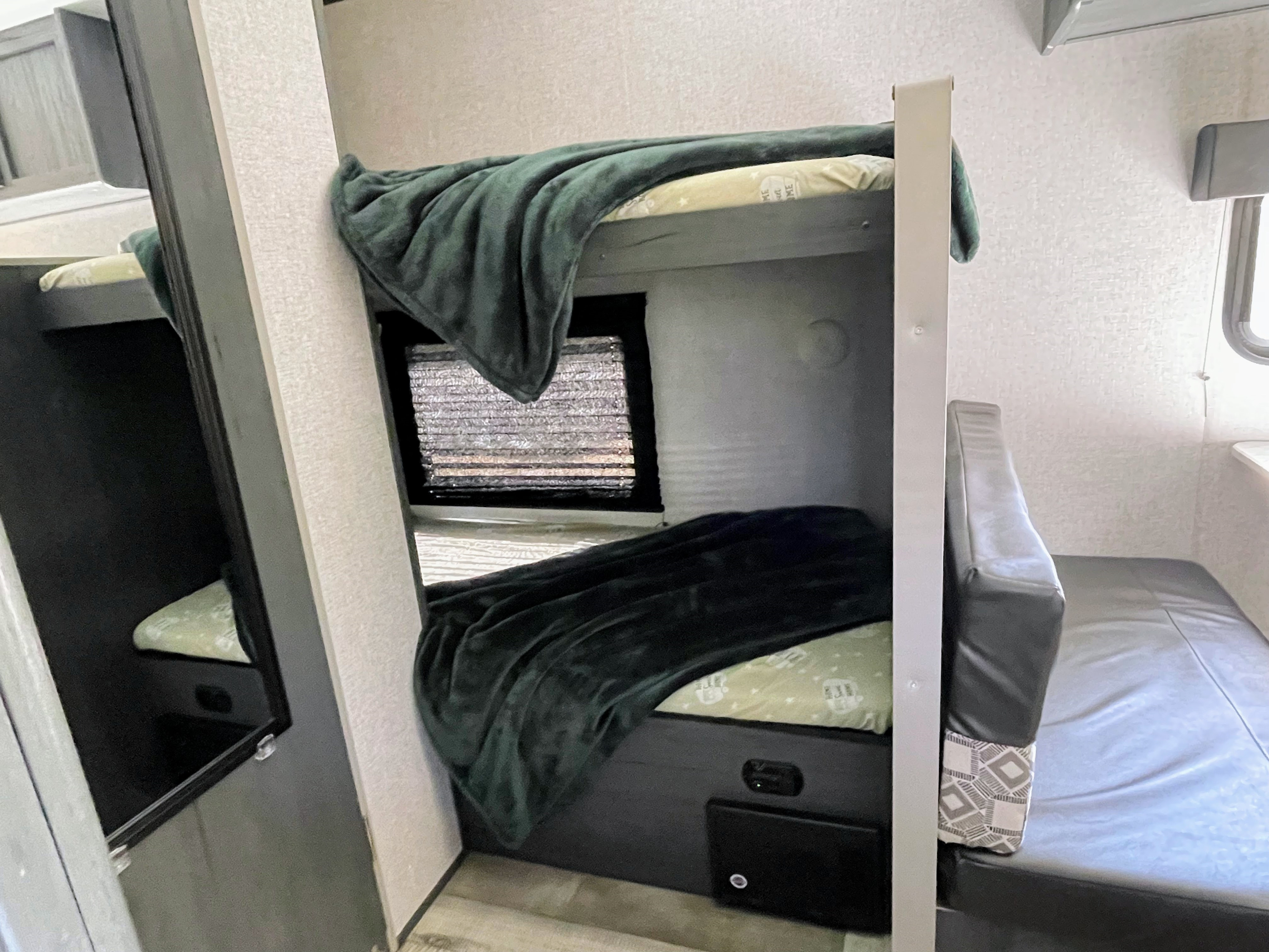 Cozy RV rental interior showing bunk beds with green blankets, a window, and a versatile sleeping/seating area.. Dutchmen Aspen Trail 2021