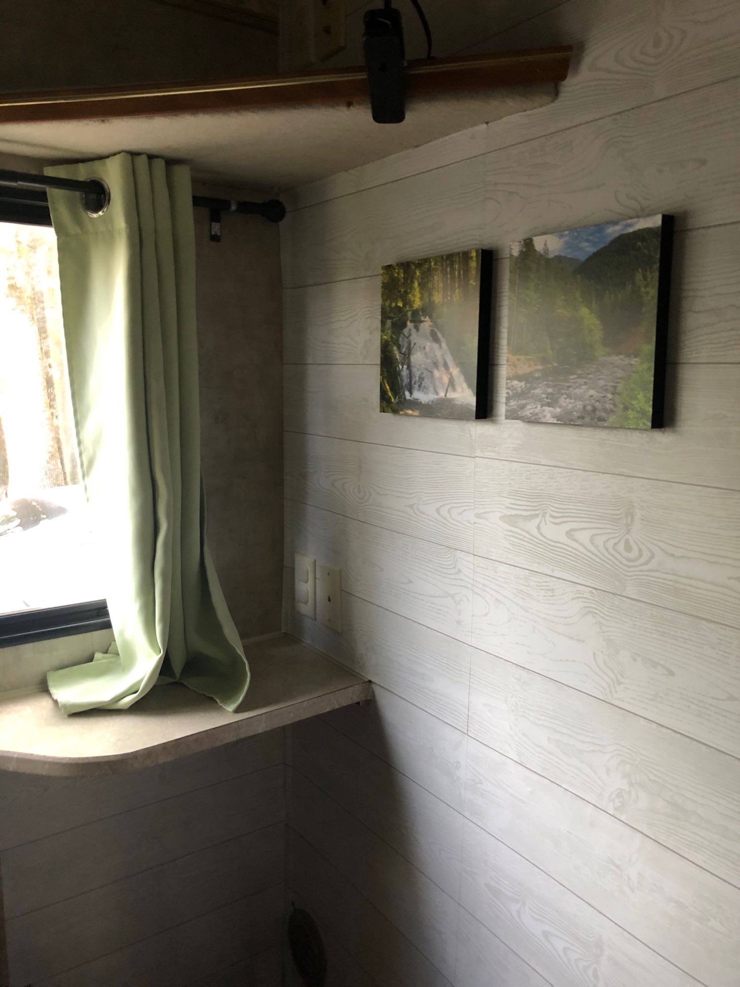 Cozy RV rental interior featuring a window with light green curtains, light wood-paneled walls, and nature art.. Fleetwood Other 2007