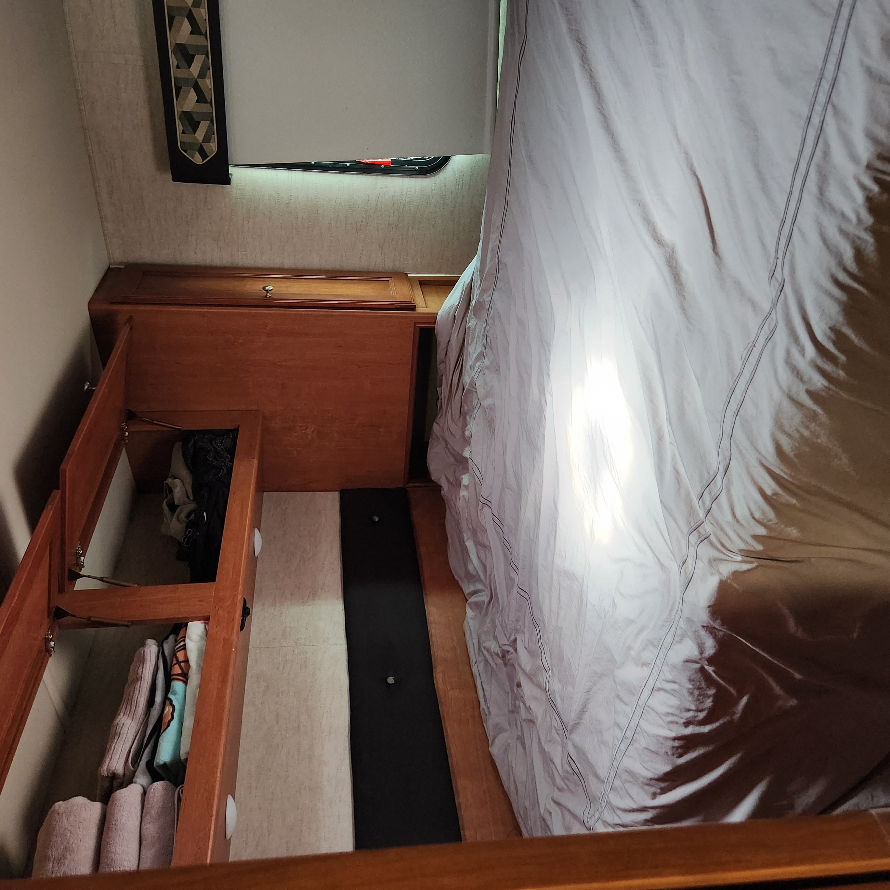 RV rental bedroom with neat bed & integrated storage. Open cabinet reveals folded laundry. Window visible.. Winnebago Vista 2017