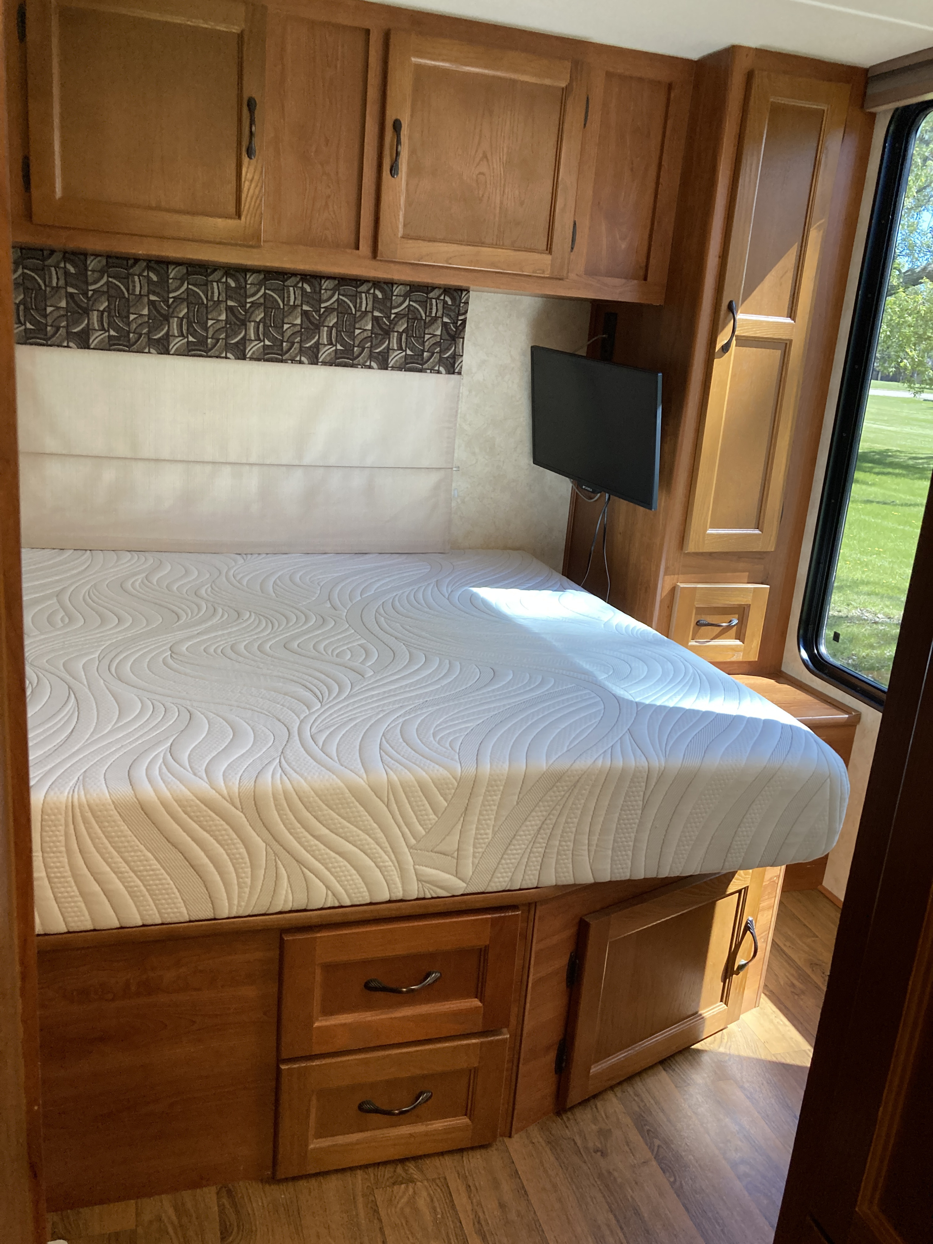 Cozy RV rental bedroom featuring a comfortable mattress, overhead cabinets, TV, and built-in storage.. Coachman Freelander 27QB 2011