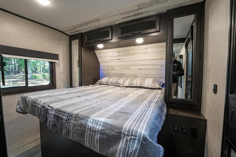 Inside an **rv rental** bedroom: a cozy bed with striped linens, overhead storage, and a window view, perfect for travel.. Jayco Jay Feather 2021