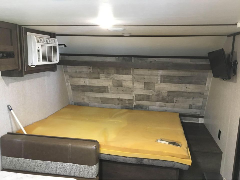 RV rental bedroom interior with yellow foam bed, wall-mounted AC, and TV for a comfortable travel stay.. Dutchmen Coleman Lantern LT 2020