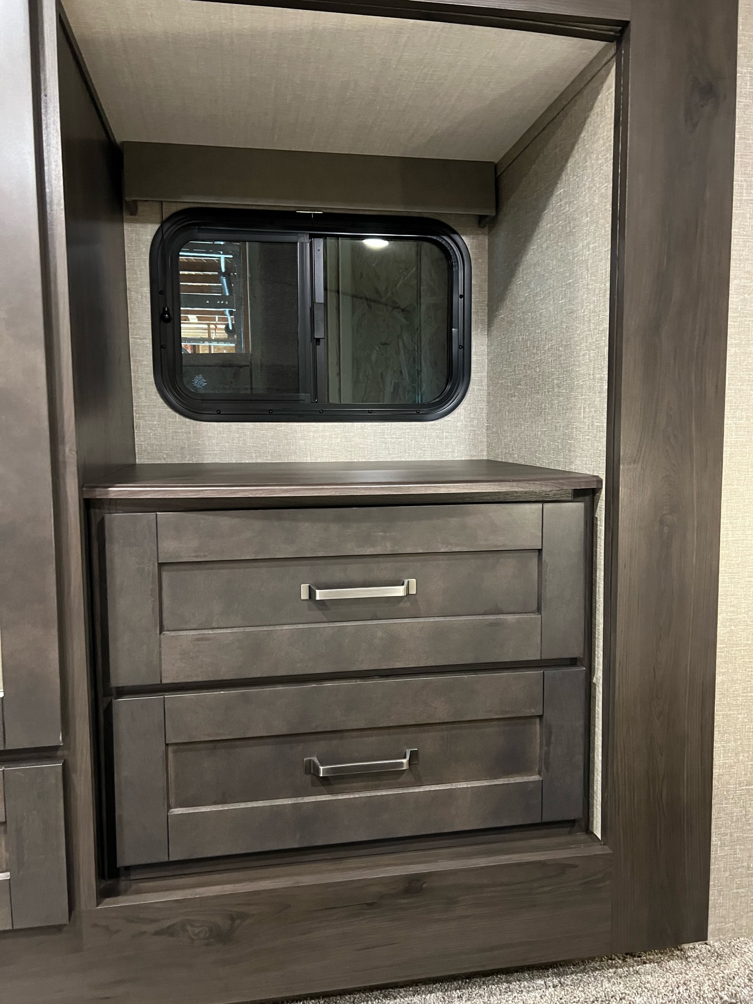Explore the practical interior of this RV rental, featuring built-in dark wood cabinetry, a two-drawer dresser, and a small window.. Grand Design Reflection 2021