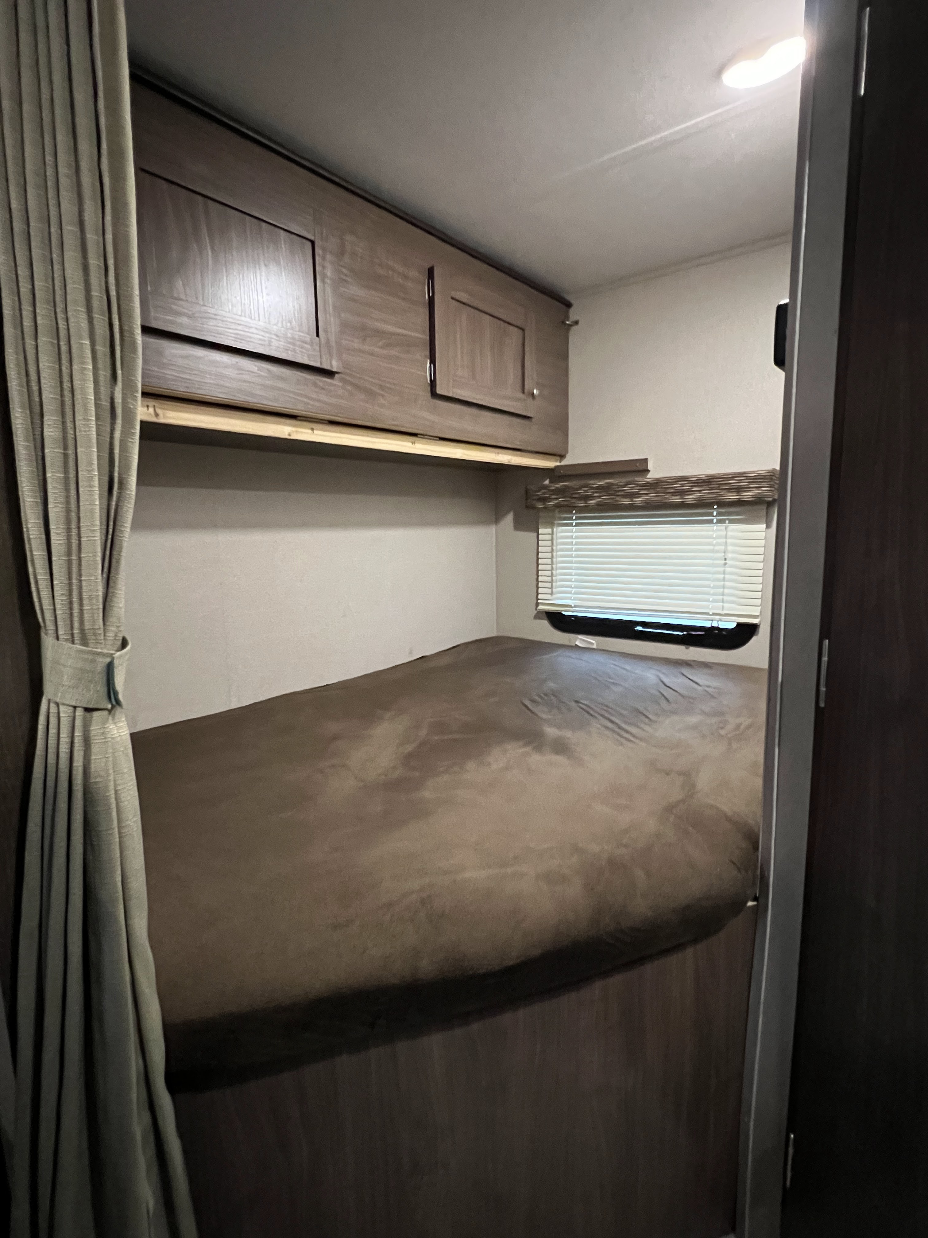 This rv rental's comfy bunk bed area features wooden overhead cabinets, a window with blinds, and tied-back privacy curtains.. Keystone RV Hideout 2018