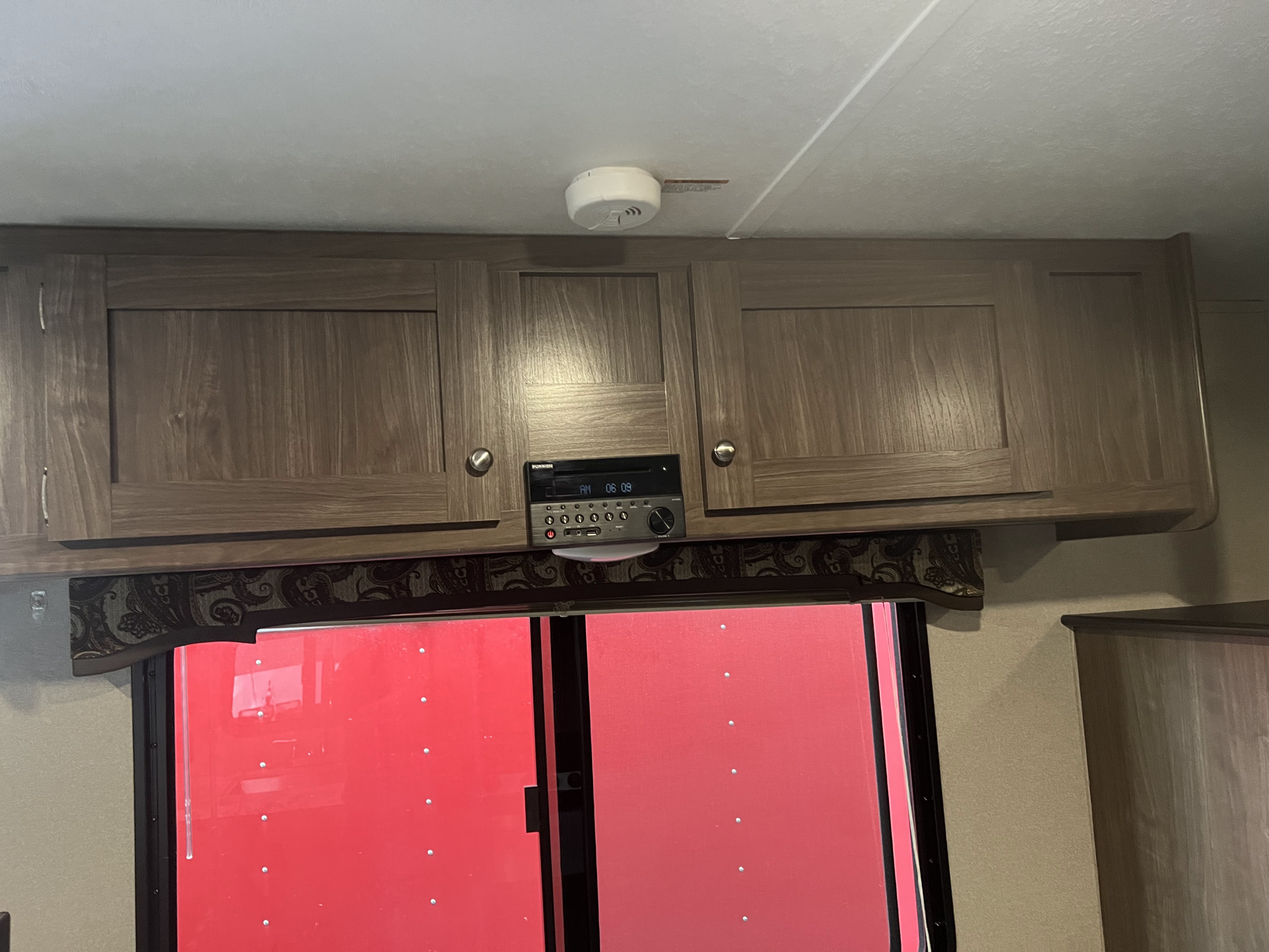 RV rental: Overhead wood cabinets, stereo system, ceiling smoke detector, and a window with patterned valance.. Keystone RV Hideout 2018