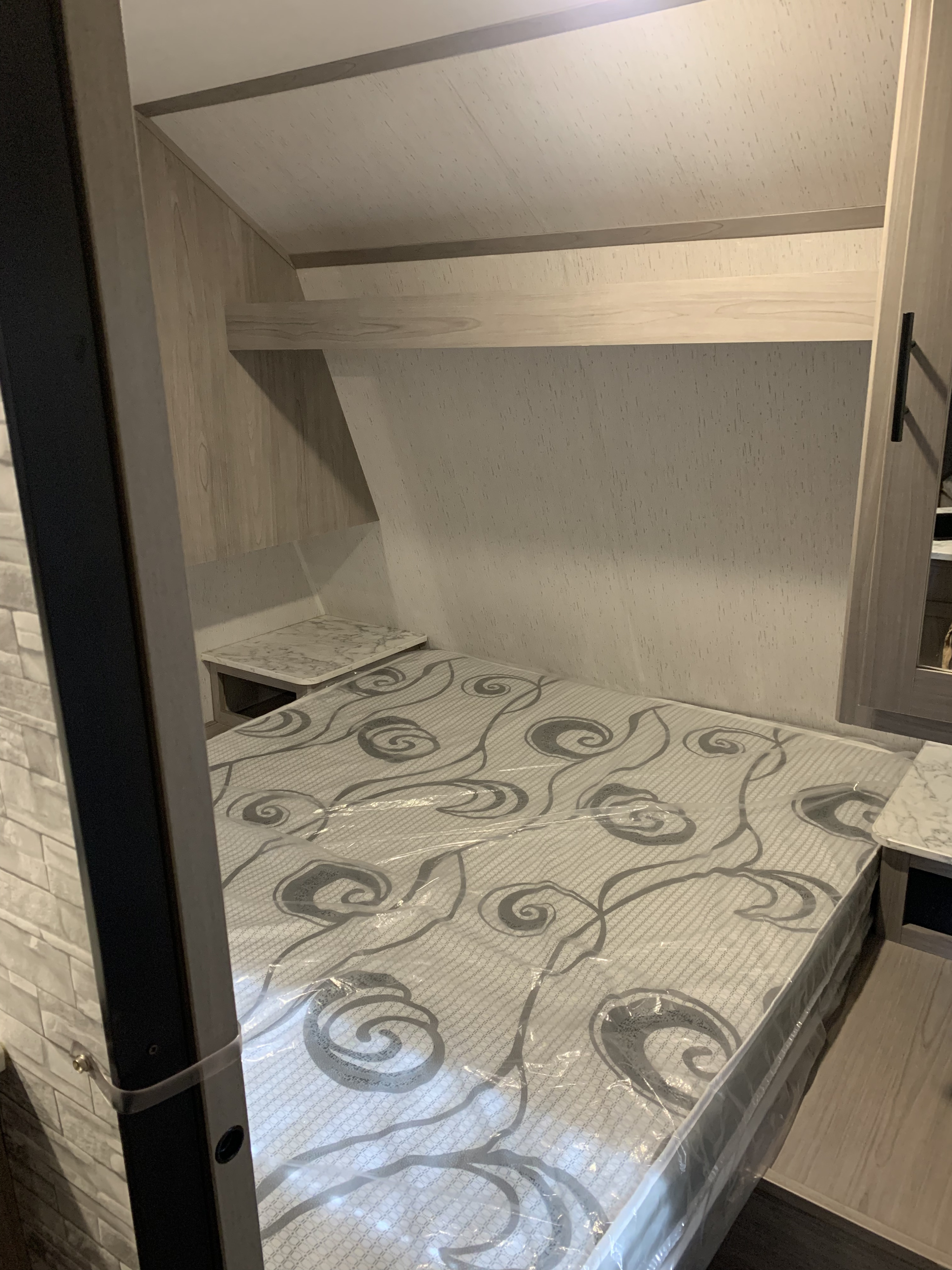 Clean rv rental bedroom featuring a new, plastic-covered mattress, side tables, and overhead shelves.. Coleman lantern 2022