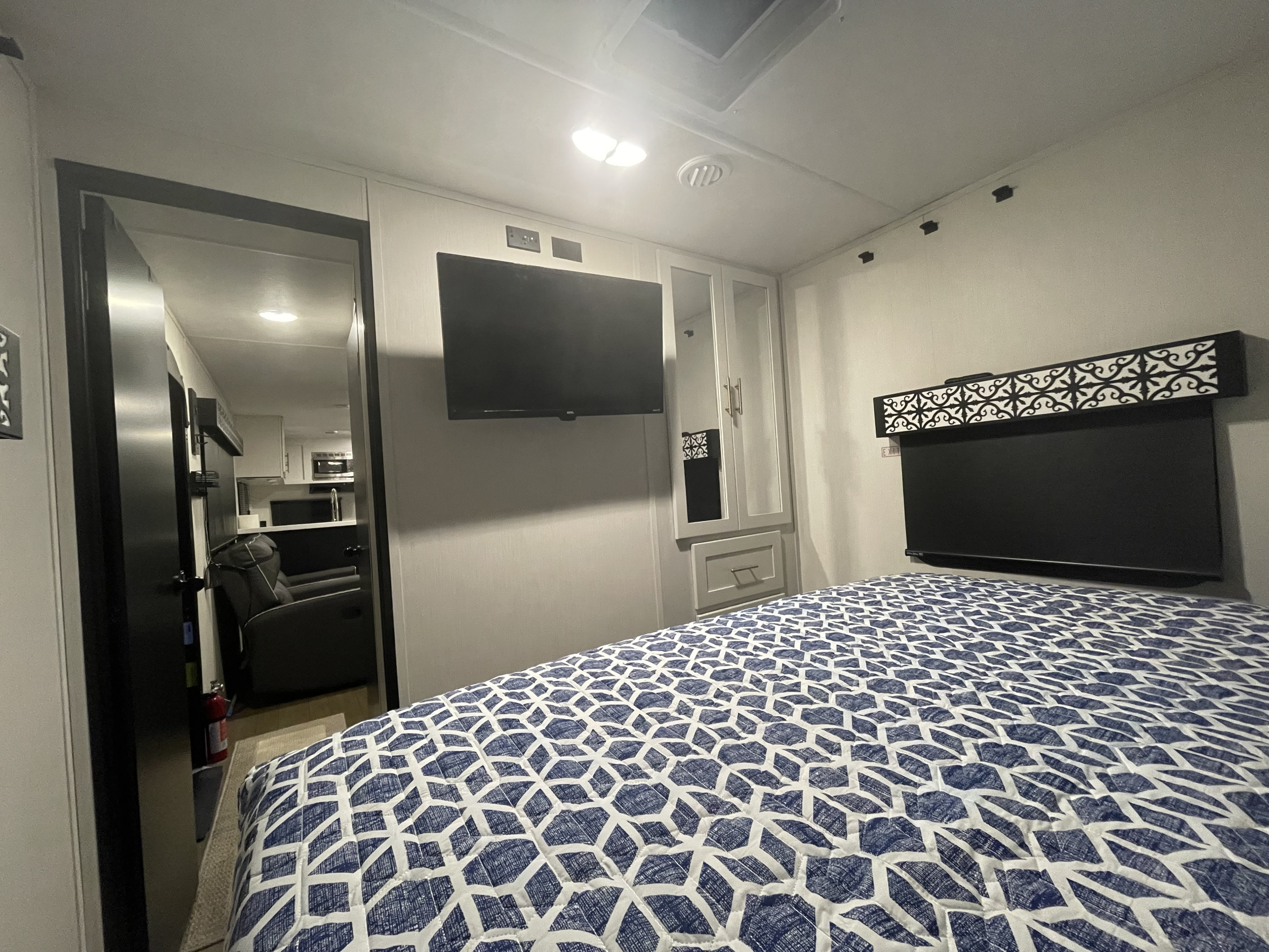 Modern RV rental interior: cozy bedroom with patterned bedding, TV, and a peek into the compact living area.. Forest River Wildcat 2022