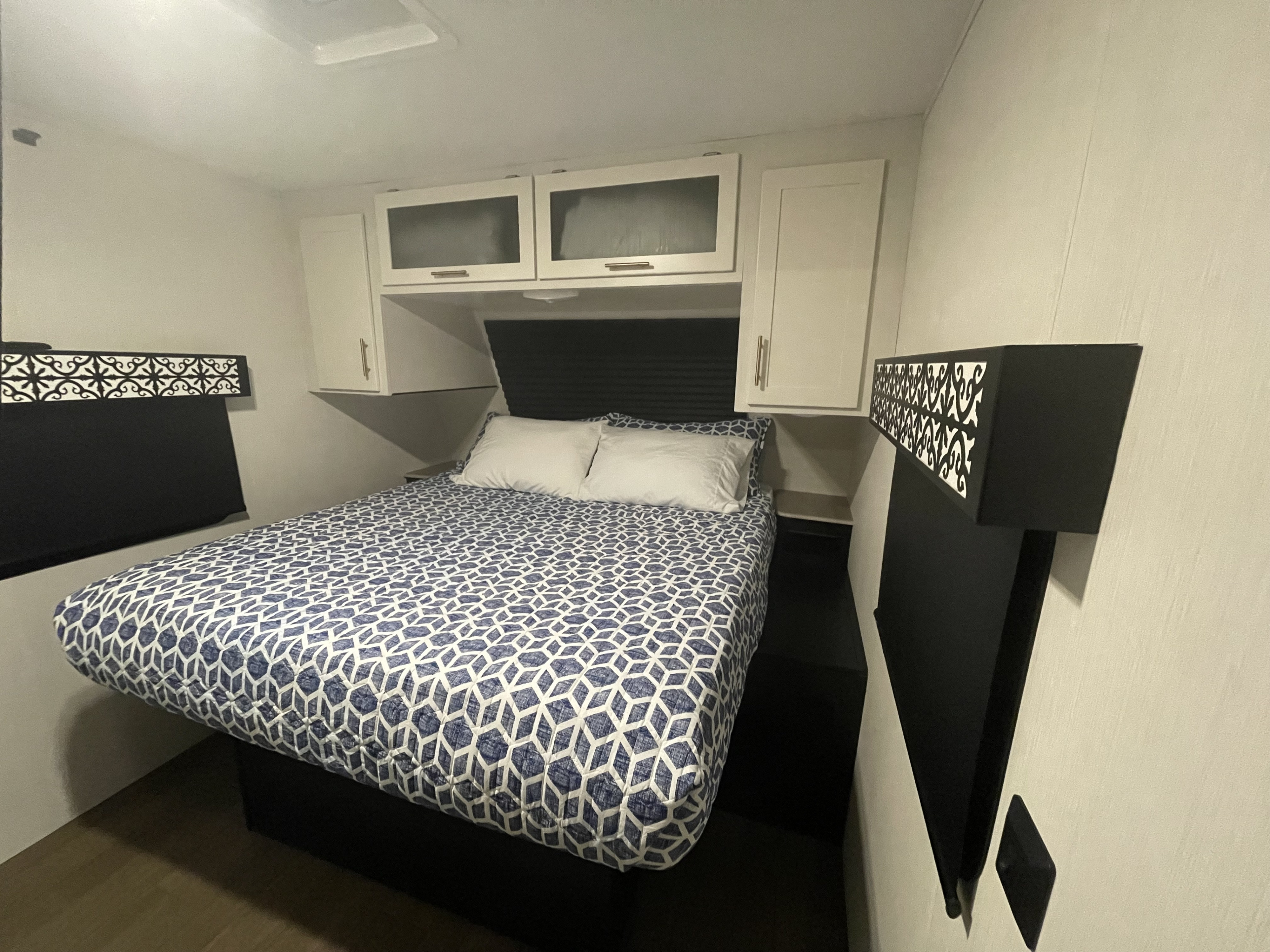 An inviting RV rental bedroom with a blue patterned bed, white cabinets, and black decorative valances.. Forest River Wildcat 2022