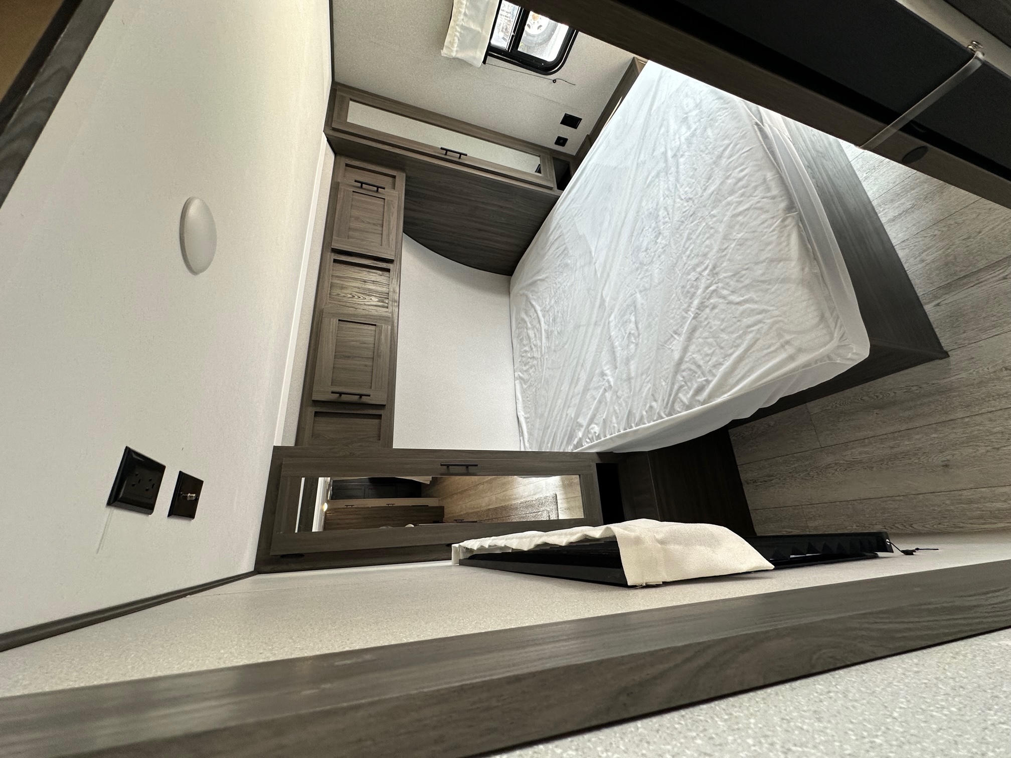 Clean, modern RV rental interior: bedroom features a bed with white sheets, wood cabinets, and power outlets.. Grand River Grand River 33BOK 2021